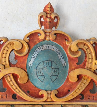 Zdjęcie nr 122: Umeblowanie zakrystii usytuowane jest wzdłuż ścian północnej, południowej i wschodniej pomieszczenia.  Na ścianie północnej, w części dolnej znajdują się trzy połączone ze sobą komody, każda o czterech szufladach, nakryte jednym blatem. W części górnej mieszczą się pięcioosiowe szafki z szufladami w cokole. Osie artykułowe są pilastrami hermowymi. Na osi środkowej szafka jest nieco wyższa i szersza z drzwiczkami dekorowanymi prostokątną, uszatą, oprofilowaną płyciną z malowanym przedstawieniem Chrystusa Eucharystycznego. Drzwiczki pozostałych szafek mają kształt stojących prostokątów i dekorowane są płycinami o wklęsłych narożach, zdobionymi gałązkami czerwonych róż, ułożonych w rokokowych wazonach. Ścianki zamknięte są niepełnym belkowaniem z gzymsem. W partii zwieńczenia osie artykułowane są cokolikami, na których ustawione są toczone, kuliste wazoniki. Pomiędzy nimi umieszczone są kartusze utworzone z ornamentu małżowinowo-chrząstkowego z malowanymi emblematami na owalnych medalionach, które ułożone są kolejno od lewej strony: 
1. Pionowo ustawiony miecz, ostrzem skierowany ku górze, połączony ze skrzyżowanymi berłem i dwoma kluczami, od których odchodzą fantazyjnie ułożone sznury w kolorze czerwonym. U góry napis na szarfie: „OBEDITE”.
2. W górnej części wyłaniająca się z chmur ręka trzymająca w dłoni węgielnicę i przymocowane do niej na łańcuszku tablice Dekalogu. Napis na szarfie: „OMNIA SVSTINET”.
3. Bóg Ojciec ukazany w półpostaci, lewą ręką opiera się na kuli ziemskiej, prawą czyni gest błogosławieństwa. 
4. Bujnie ulistnione, ciemnozielone drzewko spięte w dolnej części złotą formą w kształcie dwóch wywiniętych wolutek. Napis na szarfie: „GAVDET PATIENTIA DVRIS”. 
5. W górnej części obrazu z chmur wyłania się ręka, która zrzuca na ziemię iskrzący pocisk i dwa skrzyżowane pioruny, połączone parą białych skrzydeł. Napis „FORTIS VLTOR”.
 
Na ścianie środkowej, wschodniej znajduje się sarkofagowa mensa, powyżej parawanowa ścianka na profilowanym cokole, artykułowana pilastrami, pomiędzy którymi umieszczone są płyciny z kształcie leżących prostokątów z obrazami; ścianka zamknięta jest profilowanym gzymsem. W zwieńczeniu, na jej skrajach znajdują się owalne medaliony ujęte w kartusze z ornamentu małżowinowo-chrząstkowego. W medalionie po lewej stronie namalowane są litery alfa i omega na błękitnym tle oraz wstęga z napisem: „RENOVATUM A(NNO) D(OMINI) 1975”. Po prawej stronie analogiczny kartusz z literami w medalionie: „Ω / O / N” wpisane w formę krzyża, otoczonego niepełną aureolą; powyżej wstęga z napisem: „VIDENTEM AUDERE”. W płycinach obrazy przedstawiają świętych w ujęciu do pasa, zwróconych ku środkowi; od lewej:
1. Święty Demetriusz z włócznią opartą o prawy bark, ubrany w habit zakonu kanoników laterańskich od pokuty.
2. Święty Klet z aniołkiem, który trzyma w dłoni palmę męczeństwa i krzyż papieski. W prawym górnym narożu obrazu napis: „FAC HVIC SIGNO HONOREM”.
3. Święty Augustyn z gorejącym sercem na piersi i aniołkiem z łyżką i miseczką w dłoniach.
4. Święty ubrany w habit Marków, który trzyma w dłoni serce z krzyżem, podtrzymywane przez Chrystusa na obłokach – prawdopodobnie św. Cyriak, założyciel zakonu.
 
Na ścianie południowej znajduje się analogiczne umeblowanie, jak na ścianie północnej. W dolnej części dwie komody, a w miejscu trzeciej od wschodu szafka zdobiona dwiema uszatymi płycinami. Górna część mebla w przeciwieństwie do ściany północnej bez podwyższenia części środkowej. 
Na ścianie południowej:
1. Jasnobrązowa harfa na błękitnym tle i napis: „IN DOMINO”.
2. Ciemnobrązowy ptak i trzy podrywające się do lotu młode, w górnej części złote słońce i napis: „NON QUAE SVPER TERRAM.”
3. Po lewej stronie kompozycji wyłaniająca się z chmur ręka trzymająca skrzyżowane: miecz, czerwony krzyż i palmę. Napis: „NON ERVBESCO”.
4. W centrum przedstawienia krzak białej lilii o trzech rozgałęzieniach, w tle chmury w odcieniach koloru szaroniebieskiego. Napis na szarfie: „PER ARDVA DVLCIS”.
5. W lewej części kompozycji uskrzydlony jeleń, wspięty na tylnych nogach, po prawej stronie czarne i brązowe skały, w partii górnej otwarta korona, umieszczona pośrodku obłoku obwiedzionego biało-czerwonym pasem. Napis: „ET COMPREHENDATIS”.
 
W miejscu połączenia komód ścian północnej i południowej z dolną częścią konstrukcji na ścianie wschodniej znajdują się ukośnie ustawione, jednoskrzydłowe szafki o drzwiczkach dekorowanych prostokątną płyciną o wklęsłych narożach. Ścianki boczne części północnej i południowej zdobione są ukośną kratką. Powierzchnia szafek i komód pokryta jest polichromią imitującą marmur w kolorze beżowym, szarokremowym, różowym i rdzawym. Blaty malowane są farbą olejną w kolorze beżowym. Obramienia medalionów malowane w kolorze rdzawozłotym. Tło w większości medalionów w odcieniach błękitu, w górnych częściach majuskułowe napisy objaśniające przedstawienie, umieszczone w białych i półkoliście ułożonych szarfach. 