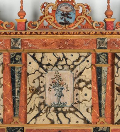 Zdjęcie nr 53: Umeblowanie zakrystii usytuowane jest wzdłuż ścian północnej, południowej i wschodniej pomieszczenia.  Na ścianie północnej, w części dolnej znajdują się trzy połączone ze sobą komody, każda o czterech szufladach, nakryte jednym blatem. W części górnej mieszczą się pięcioosiowe szafki z szufladami w cokole. Osie artykułowe są pilastrami hermowymi. Na osi środkowej szafka jest nieco wyższa i szersza z drzwiczkami dekorowanymi prostokątną, uszatą, oprofilowaną płyciną z malowanym przedstawieniem Chrystusa Eucharystycznego. Drzwiczki pozostałych szafek mają kształt stojących prostokątów i dekorowane są płycinami o wklęsłych narożach, zdobionymi gałązkami czerwonych róż, ułożonych w rokokowych wazonach. Ścianki zamknięte są niepełnym belkowaniem z gzymsem. W partii zwieńczenia osie artykułowane są cokolikami, na których ustawione są toczone, kuliste wazoniki. Pomiędzy nimi umieszczone są kartusze utworzone z ornamentu małżowinowo-chrząstkowego z malowanymi emblematami na owalnych medalionach, które ułożone są kolejno od lewej strony: 
1. Pionowo ustawiony miecz, ostrzem skierowany ku górze, połączony ze skrzyżowanymi berłem i dwoma kluczami, od których odchodzą fantazyjnie ułożone sznury w kolorze czerwonym. U góry napis na szarfie: „OBEDITE”.
2. W górnej części wyłaniająca się z chmur ręka trzymająca w dłoni węgielnicę i przymocowane do niej na łańcuszku tablice Dekalogu. Napis na szarfie: „OMNIA SVSTINET”.
3. Bóg Ojciec ukazany w półpostaci, lewą ręką opiera się na kuli ziemskiej, prawą czyni gest błogosławieństwa. 
4. Bujnie ulistnione, ciemnozielone drzewko spięte w dolnej części złotą formą w kształcie dwóch wywiniętych wolutek. Napis na szarfie: „GAVDET PATIENTIA DVRIS”. 
5. W górnej części obrazu z chmur wyłania się ręka, która zrzuca na ziemię iskrzący pocisk i dwa skrzyżowane pioruny, połączone parą białych skrzydeł. Napis „FORTIS VLTOR”.
 
Na ścianie środkowej, wschodniej znajduje się sarkofagowa mensa, powyżej parawanowa ścianka na profilowanym cokole, artykułowana pilastrami, pomiędzy którymi umieszczone są płyciny z kształcie leżących prostokątów z obrazami; ścianka zamknięta jest profilowanym gzymsem. W zwieńczeniu, na jej skrajach znajdują się owalne medaliony ujęte w kartusze z ornamentu małżowinowo-chrząstkowego. W medalionie po lewej stronie namalowane są litery alfa i omega na błękitnym tle oraz wstęga z napisem: „RENOVATUM A(NNO) D(OMINI) 1975”. Po prawej stronie analogiczny kartusz z literami w medalionie: „Ω / O / N” wpisane w formę krzyża, otoczonego niepełną aureolą; powyżej wstęga z napisem: „VIDENTEM AUDERE”. W płycinach obrazy przedstawiają świętych w ujęciu do pasa, zwróconych ku środkowi; od lewej:
1. Święty Demetriusz z włócznią opartą o prawy bark, ubrany w habit zakonu kanoników laterańskich od pokuty.
2. Święty Klet z aniołkiem, który trzyma w dłoni palmę męczeństwa i krzyż papieski. W prawym górnym narożu obrazu napis: „FAC HVIC SIGNO HONOREM”.
3. Święty Augustyn z gorejącym sercem na piersi i aniołkiem z łyżką i miseczką w dłoniach.
4. Święty ubrany w habit Marków, który trzyma w dłoni serce z krzyżem, podtrzymywane przez Chrystusa na obłokach – prawdopodobnie św. Cyriak, założyciel zakonu.
 
Na ścianie południowej znajduje się analogiczne umeblowanie, jak na ścianie północnej. W dolnej części dwie komody, a w miejscu trzeciej od wschodu szafka zdobiona dwiema uszatymi płycinami. Górna część mebla w przeciwieństwie do ściany północnej bez podwyższenia części środkowej. 
Na ścianie południowej:
1. Jasnobrązowa harfa na błękitnym tle i napis: „IN DOMINO”.
2. Ciemnobrązowy ptak i trzy podrywające się do lotu młode, w górnej części złote słońce i napis: „NON QUAE SVPER TERRAM.”
3. Po lewej stronie kompozycji wyłaniająca się z chmur ręka trzymająca skrzyżowane: miecz, czerwony krzyż i palmę. Napis: „NON ERVBESCO”.
4. W centrum przedstawienia krzak białej lilii o trzech rozgałęzieniach, w tle chmury w odcieniach koloru szaroniebieskiego. Napis na szarfie: „PER ARDVA DVLCIS”.
5. W lewej części kompozycji uskrzydlony jeleń, wspięty na tylnych nogach, po prawej stronie czarne i brązowe skały, w partii górnej otwarta korona, umieszczona pośrodku obłoku obwiedzionego biało-czerwonym pasem. Napis: „ET COMPREHENDATIS”.
 
W miejscu połączenia komód ścian północnej i południowej z dolną częścią konstrukcji na ścianie wschodniej znajdują się ukośnie ustawione, jednoskrzydłowe szafki o drzwiczkach dekorowanych prostokątną płyciną o wklęsłych narożach. Ścianki boczne części północnej i południowej zdobione są ukośną kratką. Powierzchnia szafek i komód pokryta jest polichromią imitującą marmur w kolorze beżowym, szarokremowym, różowym i rdzawym. Blaty malowane są farbą olejną w kolorze beżowym. Obramienia medalionów malowane w kolorze rdzawozłotym. Tło w większości medalionów w odcieniach błękitu, w górnych częściach majuskułowe napisy objaśniające przedstawienie, umieszczone w białych i półkoliście ułożonych szarfach. 