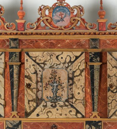 Zdjęcie nr 64: Umeblowanie zakrystii usytuowane jest wzdłuż ścian północnej, południowej i wschodniej pomieszczenia.  Na ścianie północnej, w części dolnej znajdują się trzy połączone ze sobą komody, każda o czterech szufladach, nakryte jednym blatem. W części górnej mieszczą się pięcioosiowe szafki z szufladami w cokole. Osie artykułowe są pilastrami hermowymi. Na osi środkowej szafka jest nieco wyższa i szersza z drzwiczkami dekorowanymi prostokątną, uszatą, oprofilowaną płyciną z malowanym przedstawieniem Chrystusa Eucharystycznego. Drzwiczki pozostałych szafek mają kształt stojących prostokątów i dekorowane są płycinami o wklęsłych narożach, zdobionymi gałązkami czerwonych róż, ułożonych w rokokowych wazonach. Ścianki zamknięte są niepełnym belkowaniem z gzymsem. W partii zwieńczenia osie artykułowane są cokolikami, na których ustawione są toczone, kuliste wazoniki. Pomiędzy nimi umieszczone są kartusze utworzone z ornamentu małżowinowo-chrząstkowego z malowanymi emblematami na owalnych medalionach, które ułożone są kolejno od lewej strony: 
1. Pionowo ustawiony miecz, ostrzem skierowany ku górze, połączony ze skrzyżowanymi berłem i dwoma kluczami, od których odchodzą fantazyjnie ułożone sznury w kolorze czerwonym. U góry napis na szarfie: „OBEDITE”.
2. W górnej części wyłaniająca się z chmur ręka trzymająca w dłoni węgielnicę i przymocowane do niej na łańcuszku tablice Dekalogu. Napis na szarfie: „OMNIA SVSTINET”.
3. Bóg Ojciec ukazany w półpostaci, lewą ręką opiera się na kuli ziemskiej, prawą czyni gest błogosławieństwa. 
4. Bujnie ulistnione, ciemnozielone drzewko spięte w dolnej części złotą formą w kształcie dwóch wywiniętych wolutek. Napis na szarfie: „GAVDET PATIENTIA DVRIS”. 
5. W górnej części obrazu z chmur wyłania się ręka, która zrzuca na ziemię iskrzący pocisk i dwa skrzyżowane pioruny, połączone parą białych skrzydeł. Napis „FORTIS VLTOR”.
 
Na ścianie środkowej, wschodniej znajduje się sarkofagowa mensa, powyżej parawanowa ścianka na profilowanym cokole, artykułowana pilastrami, pomiędzy którymi umieszczone są płyciny z kształcie leżących prostokątów z obrazami; ścianka zamknięta jest profilowanym gzymsem. W zwieńczeniu, na jej skrajach znajdują się owalne medaliony ujęte w kartusze z ornamentu małżowinowo-chrząstkowego. W medalionie po lewej stronie namalowane są litery alfa i omega na błękitnym tle oraz wstęga z napisem: „RENOVATUM A(NNO) D(OMINI) 1975”. Po prawej stronie analogiczny kartusz z literami w medalionie: „Ω / O / N” wpisane w formę krzyża, otoczonego niepełną aureolą; powyżej wstęga z napisem: „VIDENTEM AUDERE”. W płycinach obrazy przedstawiają świętych w ujęciu do pasa, zwróconych ku środkowi; od lewej:
1. Święty Demetriusz z włócznią opartą o prawy bark, ubrany w habit zakonu kanoników laterańskich od pokuty.
2. Święty Klet z aniołkiem, który trzyma w dłoni palmę męczeństwa i krzyż papieski. W prawym górnym narożu obrazu napis: „FAC HVIC SIGNO HONOREM”.
3. Święty Augustyn z gorejącym sercem na piersi i aniołkiem z łyżką i miseczką w dłoniach.
4. Święty ubrany w habit Marków, który trzyma w dłoni serce z krzyżem, podtrzymywane przez Chrystusa na obłokach – prawdopodobnie św. Cyriak, założyciel zakonu.
 
Na ścianie południowej znajduje się analogiczne umeblowanie, jak na ścianie północnej. W dolnej części dwie komody, a w miejscu trzeciej od wschodu szafka zdobiona dwiema uszatymi płycinami. Górna część mebla w przeciwieństwie do ściany północnej bez podwyższenia części środkowej. 
Na ścianie południowej:
1. Jasnobrązowa harfa na błękitnym tle i napis: „IN DOMINO”.
2. Ciemnobrązowy ptak i trzy podrywające się do lotu młode, w górnej części złote słońce i napis: „NON QUAE SVPER TERRAM.”
3. Po lewej stronie kompozycji wyłaniająca się z chmur ręka trzymająca skrzyżowane: miecz, czerwony krzyż i palmę. Napis: „NON ERVBESCO”.
4. W centrum przedstawienia krzak białej lilii o trzech rozgałęzieniach, w tle chmury w odcieniach koloru szaroniebieskiego. Napis na szarfie: „PER ARDVA DVLCIS”.
5. W lewej części kompozycji uskrzydlony jeleń, wspięty na tylnych nogach, po prawej stronie czarne i brązowe skały, w partii górnej otwarta korona, umieszczona pośrodku obłoku obwiedzionego biało-czerwonym pasem. Napis: „ET COMPREHENDATIS”.
 
W miejscu połączenia komód ścian północnej i południowej z dolną częścią konstrukcji na ścianie wschodniej znajdują się ukośnie ustawione, jednoskrzydłowe szafki o drzwiczkach dekorowanych prostokątną płyciną o wklęsłych narożach. Ścianki boczne części północnej i południowej zdobione są ukośną kratką. Powierzchnia szafek i komód pokryta jest polichromią imitującą marmur w kolorze beżowym, szarokremowym, różowym i rdzawym. Blaty malowane są farbą olejną w kolorze beżowym. Obramienia medalionów malowane w kolorze rdzawozłotym. Tło w większości medalionów w odcieniach błękitu, w górnych częściach majuskułowe napisy objaśniające przedstawienie, umieszczone w białych i półkoliście ułożonych szarfach. 