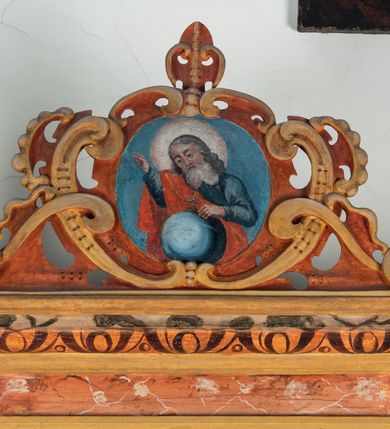 Zdjęcie nr 71: Umeblowanie zakrystii usytuowane jest wzdłuż ścian północnej, południowej i wschodniej pomieszczenia.  Na ścianie północnej, w części dolnej znajdują się trzy połączone ze sobą komody, każda o czterech szufladach, nakryte jednym blatem. W części górnej mieszczą się pięcioosiowe szafki z szufladami w cokole. Osie artykułowe są pilastrami hermowymi. Na osi środkowej szafka jest nieco wyższa i szersza z drzwiczkami dekorowanymi prostokątną, uszatą, oprofilowaną płyciną z malowanym przedstawieniem Chrystusa Eucharystycznego. Drzwiczki pozostałych szafek mają kształt stojących prostokątów i dekorowane są płycinami o wklęsłych narożach, zdobionymi gałązkami czerwonych róż, ułożonych w rokokowych wazonach. Ścianki zamknięte są niepełnym belkowaniem z gzymsem. W partii zwieńczenia osie artykułowane są cokolikami, na których ustawione są toczone, kuliste wazoniki. Pomiędzy nimi umieszczone są kartusze utworzone z ornamentu małżowinowo-chrząstkowego z malowanymi emblematami na owalnych medalionach, które ułożone są kolejno od lewej strony: 
1. Pionowo ustawiony miecz, ostrzem skierowany ku górze, połączony ze skrzyżowanymi berłem i dwoma kluczami, od których odchodzą fantazyjnie ułożone sznury w kolorze czerwonym. U góry napis na szarfie: „OBEDITE”.
2. W górnej części wyłaniająca się z chmur ręka trzymająca w dłoni węgielnicę i przymocowane do niej na łańcuszku tablice Dekalogu. Napis na szarfie: „OMNIA SVSTINET”.
3. Bóg Ojciec ukazany w półpostaci, lewą ręką opiera się na kuli ziemskiej, prawą czyni gest błogosławieństwa. 
4. Bujnie ulistnione, ciemnozielone drzewko spięte w dolnej części złotą formą w kształcie dwóch wywiniętych wolutek. Napis na szarfie: „GAVDET PATIENTIA DVRIS”. 
5. W górnej części obrazu z chmur wyłania się ręka, która zrzuca na ziemię iskrzący pocisk i dwa skrzyżowane pioruny, połączone parą białych skrzydeł. Napis „FORTIS VLTOR”.
 
Na ścianie środkowej, wschodniej znajduje się sarkofagowa mensa, powyżej parawanowa ścianka na profilowanym cokole, artykułowana pilastrami, pomiędzy którymi umieszczone są płyciny z kształcie leżących prostokątów z obrazami; ścianka zamknięta jest profilowanym gzymsem. W zwieńczeniu, na jej skrajach znajdują się owalne medaliony ujęte w kartusze z ornamentu małżowinowo-chrząstkowego. W medalionie po lewej stronie namalowane są litery alfa i omega na błękitnym tle oraz wstęga z napisem: „RENOVATUM A(NNO) D(OMINI) 1975”. Po prawej stronie analogiczny kartusz z literami w medalionie: „Ω / O / N” wpisane w formę krzyża, otoczonego niepełną aureolą; powyżej wstęga z napisem: „VIDENTEM AUDERE”. W płycinach obrazy przedstawiają świętych w ujęciu do pasa, zwróconych ku środkowi; od lewej:
1. Święty Demetriusz z włócznią opartą o prawy bark, ubrany w habit zakonu kanoników laterańskich od pokuty.
2. Święty Klet z aniołkiem, który trzyma w dłoni palmę męczeństwa i krzyż papieski. W prawym górnym narożu obrazu napis: „FAC HVIC SIGNO HONOREM”.
3. Święty Augustyn z gorejącym sercem na piersi i aniołkiem z łyżką i miseczką w dłoniach.
4. Święty ubrany w habit Marków, który trzyma w dłoni serce z krzyżem, podtrzymywane przez Chrystusa na obłokach – prawdopodobnie św. Cyriak, założyciel zakonu.
 
Na ścianie południowej znajduje się analogiczne umeblowanie, jak na ścianie północnej. W dolnej części dwie komody, a w miejscu trzeciej od wschodu szafka zdobiona dwiema uszatymi płycinami. Górna część mebla w przeciwieństwie do ściany północnej bez podwyższenia części środkowej. 
Na ścianie południowej:
1. Jasnobrązowa harfa na błękitnym tle i napis: „IN DOMINO”.
2. Ciemnobrązowy ptak i trzy podrywające się do lotu młode, w górnej części złote słońce i napis: „NON QUAE SVPER TERRAM.”
3. Po lewej stronie kompozycji wyłaniająca się z chmur ręka trzymająca skrzyżowane: miecz, czerwony krzyż i palmę. Napis: „NON ERVBESCO”.
4. W centrum przedstawienia krzak białej lilii o trzech rozgałęzieniach, w tle chmury w odcieniach koloru szaroniebieskiego. Napis na szarfie: „PER ARDVA DVLCIS”.
5. W lewej części kompozycji uskrzydlony jeleń, wspięty na tylnych nogach, po prawej stronie czarne i brązowe skały, w partii górnej otwarta korona, umieszczona pośrodku obłoku obwiedzionego biało-czerwonym pasem. Napis: „ET COMPREHENDATIS”.
 
W miejscu połączenia komód ścian północnej i południowej z dolną częścią konstrukcji na ścianie wschodniej znajdują się ukośnie ustawione, jednoskrzydłowe szafki o drzwiczkach dekorowanych prostokątną płyciną o wklęsłych narożach. Ścianki boczne części północnej i południowej zdobione są ukośną kratką. Powierzchnia szafek i komód pokryta jest polichromią imitującą marmur w kolorze beżowym, szarokremowym, różowym i rdzawym. Blaty malowane są farbą olejną w kolorze beżowym. Obramienia medalionów malowane w kolorze rdzawozłotym. Tło w większości medalionów w odcieniach błękitu, w górnych częściach majuskułowe napisy objaśniające przedstawienie, umieszczone w białych i półkoliście ułożonych szarfach. 