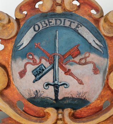 Zdjęcie nr 72: Umeblowanie zakrystii usytuowane jest wzdłuż ścian północnej, południowej i wschodniej pomieszczenia.  Na ścianie północnej, w części dolnej znajdują się trzy połączone ze sobą komody, każda o czterech szufladach, nakryte jednym blatem. W części górnej mieszczą się pięcioosiowe szafki z szufladami w cokole. Osie artykułowe są pilastrami hermowymi. Na osi środkowej szafka jest nieco wyższa i szersza z drzwiczkami dekorowanymi prostokątną, uszatą, oprofilowaną płyciną z malowanym przedstawieniem Chrystusa Eucharystycznego. Drzwiczki pozostałych szafek mają kształt stojących prostokątów i dekorowane są płycinami o wklęsłych narożach, zdobionymi gałązkami czerwonych róż, ułożonych w rokokowych wazonach. Ścianki zamknięte są niepełnym belkowaniem z gzymsem. W partii zwieńczenia osie artykułowane są cokolikami, na których ustawione są toczone, kuliste wazoniki. Pomiędzy nimi umieszczone są kartusze utworzone z ornamentu małżowinowo-chrząstkowego z malowanymi emblematami na owalnych medalionach, które ułożone są kolejno od lewej strony: 
1. Pionowo ustawiony miecz, ostrzem skierowany ku górze, połączony ze skrzyżowanymi berłem i dwoma kluczami, od których odchodzą fantazyjnie ułożone sznury w kolorze czerwonym. U góry napis na szarfie: „OBEDITE”.
2. W górnej części wyłaniająca się z chmur ręka trzymająca w dłoni węgielnicę i przymocowane do niej na łańcuszku tablice Dekalogu. Napis na szarfie: „OMNIA SVSTINET”.
3. Bóg Ojciec ukazany w półpostaci, lewą ręką opiera się na kuli ziemskiej, prawą czyni gest błogosławieństwa. 
4. Bujnie ulistnione, ciemnozielone drzewko spięte w dolnej części złotą formą w kształcie dwóch wywiniętych wolutek. Napis na szarfie: „GAVDET PATIENTIA DVRIS”. 
5. W górnej części obrazu z chmur wyłania się ręka, która zrzuca na ziemię iskrzący pocisk i dwa skrzyżowane pioruny, połączone parą białych skrzydeł. Napis „FORTIS VLTOR”.
 
Na ścianie środkowej, wschodniej znajduje się sarkofagowa mensa, powyżej parawanowa ścianka na profilowanym cokole, artykułowana pilastrami, pomiędzy którymi umieszczone są płyciny z kształcie leżących prostokątów z obrazami; ścianka zamknięta jest profilowanym gzymsem. W zwieńczeniu, na jej skrajach znajdują się owalne medaliony ujęte w kartusze z ornamentu małżowinowo-chrząstkowego. W medalionie po lewej stronie namalowane są litery alfa i omega na błękitnym tle oraz wstęga z napisem: „RENOVATUM A(NNO) D(OMINI) 1975”. Po prawej stronie analogiczny kartusz z literami w medalionie: „Ω / O / N” wpisane w formę krzyża, otoczonego niepełną aureolą; powyżej wstęga z napisem: „VIDENTEM AUDERE”. W płycinach obrazy przedstawiają świętych w ujęciu do pasa, zwróconych ku środkowi; od lewej:
1. Święty Demetriusz z włócznią opartą o prawy bark, ubrany w habit zakonu kanoników laterańskich od pokuty.
2. Święty Klet z aniołkiem, który trzyma w dłoni palmę męczeństwa i krzyż papieski. W prawym górnym narożu obrazu napis: „FAC HVIC SIGNO HONOREM”.
3. Święty Augustyn z gorejącym sercem na piersi i aniołkiem z łyżką i miseczką w dłoniach.
4. Święty ubrany w habit Marków, który trzyma w dłoni serce z krzyżem, podtrzymywane przez Chrystusa na obłokach – prawdopodobnie św. Cyriak, założyciel zakonu.
 
Na ścianie południowej znajduje się analogiczne umeblowanie, jak na ścianie północnej. W dolnej części dwie komody, a w miejscu trzeciej od wschodu szafka zdobiona dwiema uszatymi płycinami. Górna część mebla w przeciwieństwie do ściany północnej bez podwyższenia części środkowej. 
Na ścianie południowej:
1. Jasnobrązowa harfa na błękitnym tle i napis: „IN DOMINO”.
2. Ciemnobrązowy ptak i trzy podrywające się do lotu młode, w górnej części złote słońce i napis: „NON QUAE SVPER TERRAM.”
3. Po lewej stronie kompozycji wyłaniająca się z chmur ręka trzymająca skrzyżowane: miecz, czerwony krzyż i palmę. Napis: „NON ERVBESCO”.
4. W centrum przedstawienia krzak białej lilii o trzech rozgałęzieniach, w tle chmury w odcieniach koloru szaroniebieskiego. Napis na szarfie: „PER ARDVA DVLCIS”.
5. W lewej części kompozycji uskrzydlony jeleń, wspięty na tylnych nogach, po prawej stronie czarne i brązowe skały, w partii górnej otwarta korona, umieszczona pośrodku obłoku obwiedzionego biało-czerwonym pasem. Napis: „ET COMPREHENDATIS”.
 
W miejscu połączenia komód ścian północnej i południowej z dolną częścią konstrukcji na ścianie wschodniej znajdują się ukośnie ustawione, jednoskrzydłowe szafki o drzwiczkach dekorowanych prostokątną płyciną o wklęsłych narożach. Ścianki boczne części północnej i południowej zdobione są ukośną kratką. Powierzchnia szafek i komód pokryta jest polichromią imitującą marmur w kolorze beżowym, szarokremowym, różowym i rdzawym. Blaty malowane są farbą olejną w kolorze beżowym. Obramienia medalionów malowane w kolorze rdzawozłotym. Tło w większości medalionów w odcieniach błękitu, w górnych częściach majuskułowe napisy objaśniające przedstawienie, umieszczone w białych i półkoliście ułożonych szarfach. 