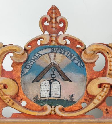 Zdjęcie nr 80: Umeblowanie zakrystii usytuowane jest wzdłuż ścian północnej, południowej i wschodniej pomieszczenia.  Na ścianie północnej, w części dolnej znajdują się trzy połączone ze sobą komody, każda o czterech szufladach, nakryte jednym blatem. W części górnej mieszczą się pięcioosiowe szafki z szufladami w cokole. Osie artykułowe są pilastrami hermowymi. Na osi środkowej szafka jest nieco wyższa i szersza z drzwiczkami dekorowanymi prostokątną, uszatą, oprofilowaną płyciną z malowanym przedstawieniem Chrystusa Eucharystycznego. Drzwiczki pozostałych szafek mają kształt stojących prostokątów i dekorowane są płycinami o wklęsłych narożach, zdobionymi gałązkami czerwonych róż, ułożonych w rokokowych wazonach. Ścianki zamknięte są niepełnym belkowaniem z gzymsem. W partii zwieńczenia osie artykułowane są cokolikami, na których ustawione są toczone, kuliste wazoniki. Pomiędzy nimi umieszczone są kartusze utworzone z ornamentu małżowinowo-chrząstkowego z malowanymi emblematami na owalnych medalionach, które ułożone są kolejno od lewej strony: 
1. Pionowo ustawiony miecz, ostrzem skierowany ku górze, połączony ze skrzyżowanymi berłem i dwoma kluczami, od których odchodzą fantazyjnie ułożone sznury w kolorze czerwonym. U góry napis na szarfie: „OBEDITE”.
2. W górnej części wyłaniająca się z chmur ręka trzymająca w dłoni węgielnicę i przymocowane do niej na łańcuszku tablice Dekalogu. Napis na szarfie: „OMNIA SVSTINET”.
3. Bóg Ojciec ukazany w półpostaci, lewą ręką opiera się na kuli ziemskiej, prawą czyni gest błogosławieństwa. 
4. Bujnie ulistnione, ciemnozielone drzewko spięte w dolnej części złotą formą w kształcie dwóch wywiniętych wolutek. Napis na szarfie: „GAVDET PATIENTIA DVRIS”. 
5. W górnej części obrazu z chmur wyłania się ręka, która zrzuca na ziemię iskrzący pocisk i dwa skrzyżowane pioruny, połączone parą białych skrzydeł. Napis „FORTIS VLTOR”.
 
Na ścianie środkowej, wschodniej znajduje się sarkofagowa mensa, powyżej parawanowa ścianka na profilowanym cokole, artykułowana pilastrami, pomiędzy którymi umieszczone są płyciny z kształcie leżących prostokątów z obrazami; ścianka zamknięta jest profilowanym gzymsem. W zwieńczeniu, na jej skrajach znajdują się owalne medaliony ujęte w kartusze z ornamentu małżowinowo-chrząstkowego. W medalionie po lewej stronie namalowane są litery alfa i omega na błękitnym tle oraz wstęga z napisem: „RENOVATUM A(NNO) D(OMINI) 1975”. Po prawej stronie analogiczny kartusz z literami w medalionie: „Ω / O / N” wpisane w formę krzyża, otoczonego niepełną aureolą; powyżej wstęga z napisem: „VIDENTEM AUDERE”. W płycinach obrazy przedstawiają świętych w ujęciu do pasa, zwróconych ku środkowi; od lewej:
1. Święty Demetriusz z włócznią opartą o prawy bark, ubrany w habit zakonu kanoników laterańskich od pokuty.
2. Święty Klet z aniołkiem, który trzyma w dłoni palmę męczeństwa i krzyż papieski. W prawym górnym narożu obrazu napis: „FAC HVIC SIGNO HONOREM”.
3. Święty Augustyn z gorejącym sercem na piersi i aniołkiem z łyżką i miseczką w dłoniach.
4. Święty ubrany w habit Marków, który trzyma w dłoni serce z krzyżem, podtrzymywane przez Chrystusa na obłokach – prawdopodobnie św. Cyriak, założyciel zakonu.
 
Na ścianie południowej znajduje się analogiczne umeblowanie, jak na ścianie północnej. W dolnej części dwie komody, a w miejscu trzeciej od wschodu szafka zdobiona dwiema uszatymi płycinami. Górna część mebla w przeciwieństwie do ściany północnej bez podwyższenia części środkowej. 
Na ścianie południowej:
1. Jasnobrązowa harfa na błękitnym tle i napis: „IN DOMINO”.
2. Ciemnobrązowy ptak i trzy podrywające się do lotu młode, w górnej części złote słońce i napis: „NON QUAE SVPER TERRAM.”
3. Po lewej stronie kompozycji wyłaniająca się z chmur ręka trzymająca skrzyżowane: miecz, czerwony krzyż i palmę. Napis: „NON ERVBESCO”.
4. W centrum przedstawienia krzak białej lilii o trzech rozgałęzieniach, w tle chmury w odcieniach koloru szaroniebieskiego. Napis na szarfie: „PER ARDVA DVLCIS”.
5. W lewej części kompozycji uskrzydlony jeleń, wspięty na tylnych nogach, po prawej stronie czarne i brązowe skały, w partii górnej otwarta korona, umieszczona pośrodku obłoku obwiedzionego biało-czerwonym pasem. Napis: „ET COMPREHENDATIS”.
 
W miejscu połączenia komód ścian północnej i południowej z dolną częścią konstrukcji na ścianie wschodniej znajdują się ukośnie ustawione, jednoskrzydłowe szafki o drzwiczkach dekorowanych prostokątną płyciną o wklęsłych narożach. Ścianki boczne części północnej i południowej zdobione są ukośną kratką. Powierzchnia szafek i komód pokryta jest polichromią imitującą marmur w kolorze beżowym, szarokremowym, różowym i rdzawym. Blaty malowane są farbą olejną w kolorze beżowym. Obramienia medalionów malowane w kolorze rdzawozłotym. Tło w większości medalionów w odcieniach błękitu, w górnych częściach majuskułowe napisy objaśniające przedstawienie, umieszczone w białych i półkoliście ułożonych szarfach. 