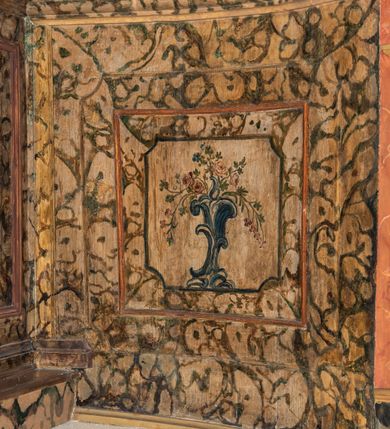 Zdjęcie nr 103: Umeblowanie zakrystii usytuowane jest wzdłuż ścian północnej, południowej i wschodniej pomieszczenia.  Na ścianie północnej, w części dolnej znajdują się trzy połączone ze sobą komody, każda o czterech szufladach, nakryte jednym blatem. W części górnej mieszczą się pięcioosiowe szafki z szufladami w cokole. Osie artykułowe są pilastrami hermowymi. Na osi środkowej szafka jest nieco wyższa i szersza z drzwiczkami dekorowanymi prostokątną, uszatą, oprofilowaną płyciną z malowanym przedstawieniem Chrystusa Eucharystycznego. Drzwiczki pozostałych szafek mają kształt stojących prostokątów i dekorowane są płycinami o wklęsłych narożach, zdobionymi gałązkami czerwonych róż, ułożonych w rokokowych wazonach. Ścianki zamknięte są niepełnym belkowaniem z gzymsem. W partii zwieńczenia osie artykułowane są cokolikami, na których ustawione są toczone, kuliste wazoniki. Pomiędzy nimi umieszczone są kartusze utworzone z ornamentu małżowinowo-chrząstkowego z malowanymi emblematami na owalnych medalionach, które ułożone są kolejno od lewej strony: 
1. Pionowo ustawiony miecz, ostrzem skierowany ku górze, połączony ze skrzyżowanymi berłem i dwoma kluczami, od których odchodzą fantazyjnie ułożone sznury w kolorze czerwonym. U góry napis na szarfie: „OBEDITE”.
2. W górnej części wyłaniająca się z chmur ręka trzymająca w dłoni węgielnicę i przymocowane do niej na łańcuszku tablice Dekalogu. Napis na szarfie: „OMNIA SVSTINET”.
3. Bóg Ojciec ukazany w półpostaci, lewą ręką opiera się na kuli ziemskiej, prawą czyni gest błogosławieństwa. 
4. Bujnie ulistnione, ciemnozielone drzewko spięte w dolnej części złotą formą w kształcie dwóch wywiniętych wolutek. Napis na szarfie: „GAVDET PATIENTIA DVRIS”. 
5. W górnej części obrazu z chmur wyłania się ręka, która zrzuca na ziemię iskrzący pocisk i dwa skrzyżowane pioruny, połączone parą białych skrzydeł. Napis „FORTIS VLTOR”.
 
Na ścianie środkowej, wschodniej znajduje się sarkofagowa mensa, powyżej parawanowa ścianka na profilowanym cokole, artykułowana pilastrami, pomiędzy którymi umieszczone są płyciny z kształcie leżących prostokątów z obrazami; ścianka zamknięta jest profilowanym gzymsem. W zwieńczeniu, na jej skrajach znajdują się owalne medaliony ujęte w kartusze z ornamentu małżowinowo-chrząstkowego. W medalionie po lewej stronie namalowane są litery alfa i omega na błękitnym tle oraz wstęga z napisem: „RENOVATUM A(NNO) D(OMINI) 1975”. Po prawej stronie analogiczny kartusz z literami w medalionie: „Ω / O / N” wpisane w formę krzyża, otoczonego niepełną aureolą; powyżej wstęga z napisem: „VIDENTEM AUDERE”. W płycinach obrazy przedstawiają świętych w ujęciu do pasa, zwróconych ku środkowi; od lewej:
1. Święty Demetriusz z włócznią opartą o prawy bark, ubrany w habit zakonu kanoników laterańskich od pokuty.
2. Święty Klet z aniołkiem, który trzyma w dłoni palmę męczeństwa i krzyż papieski. W prawym górnym narożu obrazu napis: „FAC HVIC SIGNO HONOREM”.
3. Święty Augustyn z gorejącym sercem na piersi i aniołkiem z łyżką i miseczką w dłoniach.
4. Święty ubrany w habit Marków, który trzyma w dłoni serce z krzyżem, podtrzymywane przez Chrystusa na obłokach – prawdopodobnie św. Cyriak, założyciel zakonu.
 
Na ścianie południowej znajduje się analogiczne umeblowanie, jak na ścianie północnej. W dolnej części dwie komody, a w miejscu trzeciej od wschodu szafka zdobiona dwiema uszatymi płycinami. Górna część mebla w przeciwieństwie do ściany północnej bez podwyższenia części środkowej. 
Na ścianie południowej:
1. Jasnobrązowa harfa na błękitnym tle i napis: „IN DOMINO”.
2. Ciemnobrązowy ptak i trzy podrywające się do lotu młode, w górnej części złote słońce i napis: „NON QUAE SVPER TERRAM.”
3. Po lewej stronie kompozycji wyłaniająca się z chmur ręka trzymająca skrzyżowane: miecz, czerwony krzyż i palmę. Napis: „NON ERVBESCO”.
4. W centrum przedstawienia krzak białej lilii o trzech rozgałęzieniach, w tle chmury w odcieniach koloru szaroniebieskiego. Napis na szarfie: „PER ARDVA DVLCIS”.
5. W lewej części kompozycji uskrzydlony jeleń, wspięty na tylnych nogach, po prawej stronie czarne i brązowe skały, w partii górnej otwarta korona, umieszczona pośrodku obłoku obwiedzionego biało-czerwonym pasem. Napis: „ET COMPREHENDATIS”.
 
W miejscu połączenia komód ścian północnej i południowej z dolną częścią konstrukcji na ścianie wschodniej znajdują się ukośnie ustawione, jednoskrzydłowe szafki o drzwiczkach dekorowanych prostokątną płyciną o wklęsłych narożach. Ścianki boczne części północnej i południowej zdobione są ukośną kratką. Powierzchnia szafek i komód pokryta jest polichromią imitującą marmur w kolorze beżowym, szarokremowym, różowym i rdzawym. Blaty malowane są farbą olejną w kolorze beżowym. Obramienia medalionów malowane w kolorze rdzawozłotym. Tło w większości medalionów w odcieniach błękitu, w górnych częściach majuskułowe napisy objaśniające przedstawienie, umieszczone w białych i półkoliście ułożonych szarfach. 