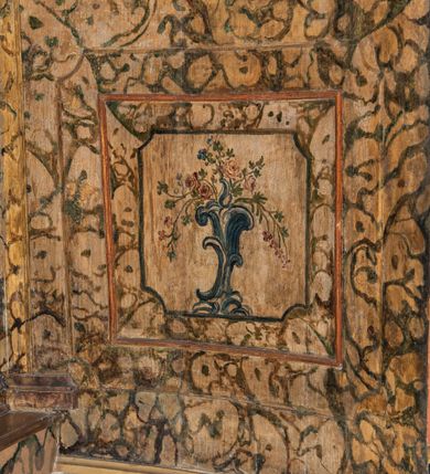 Zdjęcie nr 107: Umeblowanie zakrystii usytuowane jest wzdłuż ścian północnej, południowej i wschodniej pomieszczenia.  Na ścianie północnej, w części dolnej znajdują się trzy połączone ze sobą komody, każda o czterech szufladach, nakryte jednym blatem. W części górnej mieszczą się pięcioosiowe szafki z szufladami w cokole. Osie artykułowe są pilastrami hermowymi. Na osi środkowej szafka jest nieco wyższa i szersza z drzwiczkami dekorowanymi prostokątną, uszatą, oprofilowaną płyciną z malowanym przedstawieniem Chrystusa Eucharystycznego. Drzwiczki pozostałych szafek mają kształt stojących prostokątów i dekorowane są płycinami o wklęsłych narożach, zdobionymi gałązkami czerwonych róż, ułożonych w rokokowych wazonach. Ścianki zamknięte są niepełnym belkowaniem z gzymsem. W partii zwieńczenia osie artykułowane są cokolikami, na których ustawione są toczone, kuliste wazoniki. Pomiędzy nimi umieszczone są kartusze utworzone z ornamentu małżowinowo-chrząstkowego z malowanymi emblematami na owalnych medalionach, które ułożone są kolejno od lewej strony: 
1. Pionowo ustawiony miecz, ostrzem skierowany ku górze, połączony ze skrzyżowanymi berłem i dwoma kluczami, od których odchodzą fantazyjnie ułożone sznury w kolorze czerwonym. U góry napis na szarfie: „OBEDITE”.
2. W górnej części wyłaniająca się z chmur ręka trzymająca w dłoni węgielnicę i przymocowane do niej na łańcuszku tablice Dekalogu. Napis na szarfie: „OMNIA SVSTINET”.
3. Bóg Ojciec ukazany w półpostaci, lewą ręką opiera się na kuli ziemskiej, prawą czyni gest błogosławieństwa. 
4. Bujnie ulistnione, ciemnozielone drzewko spięte w dolnej części złotą formą w kształcie dwóch wywiniętych wolutek. Napis na szarfie: „GAVDET PATIENTIA DVRIS”. 
5. W górnej części obrazu z chmur wyłania się ręka, która zrzuca na ziemię iskrzący pocisk i dwa skrzyżowane pioruny, połączone parą białych skrzydeł. Napis „FORTIS VLTOR”.
 
Na ścianie środkowej, wschodniej znajduje się sarkofagowa mensa, powyżej parawanowa ścianka na profilowanym cokole, artykułowana pilastrami, pomiędzy którymi umieszczone są płyciny z kształcie leżących prostokątów z obrazami; ścianka zamknięta jest profilowanym gzymsem. W zwieńczeniu, na jej skrajach znajdują się owalne medaliony ujęte w kartusze z ornamentu małżowinowo-chrząstkowego. W medalionie po lewej stronie namalowane są litery alfa i omega na błękitnym tle oraz wstęga z napisem: „RENOVATUM A(NNO) D(OMINI) 1975”. Po prawej stronie analogiczny kartusz z literami w medalionie: „Ω / O / N” wpisane w formę krzyża, otoczonego niepełną aureolą; powyżej wstęga z napisem: „VIDENTEM AUDERE”. W płycinach obrazy przedstawiają świętych w ujęciu do pasa, zwróconych ku środkowi; od lewej:
1. Święty Demetriusz z włócznią opartą o prawy bark, ubrany w habit zakonu kanoników laterańskich od pokuty.
2. Święty Klet z aniołkiem, który trzyma w dłoni palmę męczeństwa i krzyż papieski. W prawym górnym narożu obrazu napis: „FAC HVIC SIGNO HONOREM”.
3. Święty Augustyn z gorejącym sercem na piersi i aniołkiem z łyżką i miseczką w dłoniach.
4. Święty ubrany w habit Marków, który trzyma w dłoni serce z krzyżem, podtrzymywane przez Chrystusa na obłokach – prawdopodobnie św. Cyriak, założyciel zakonu.
 
Na ścianie południowej znajduje się analogiczne umeblowanie, jak na ścianie północnej. W dolnej części dwie komody, a w miejscu trzeciej od wschodu szafka zdobiona dwiema uszatymi płycinami. Górna część mebla w przeciwieństwie do ściany północnej bez podwyższenia części środkowej. 
Na ścianie południowej:
1. Jasnobrązowa harfa na błękitnym tle i napis: „IN DOMINO”.
2. Ciemnobrązowy ptak i trzy podrywające się do lotu młode, w górnej części złote słońce i napis: „NON QUAE SVPER TERRAM.”
3. Po lewej stronie kompozycji wyłaniająca się z chmur ręka trzymająca skrzyżowane: miecz, czerwony krzyż i palmę. Napis: „NON ERVBESCO”.
4. W centrum przedstawienia krzak białej lilii o trzech rozgałęzieniach, w tle chmury w odcieniach koloru szaroniebieskiego. Napis na szarfie: „PER ARDVA DVLCIS”.
5. W lewej części kompozycji uskrzydlony jeleń, wspięty na tylnych nogach, po prawej stronie czarne i brązowe skały, w partii górnej otwarta korona, umieszczona pośrodku obłoku obwiedzionego biało-czerwonym pasem. Napis: „ET COMPREHENDATIS”.
 
W miejscu połączenia komód ścian północnej i południowej z dolną częścią konstrukcji na ścianie wschodniej znajdują się ukośnie ustawione, jednoskrzydłowe szafki o drzwiczkach dekorowanych prostokątną płyciną o wklęsłych narożach. Ścianki boczne części północnej i południowej zdobione są ukośną kratką. Powierzchnia szafek i komód pokryta jest polichromią imitującą marmur w kolorze beżowym, szarokremowym, różowym i rdzawym. Blaty malowane są farbą olejną w kolorze beżowym. Obramienia medalionów malowane w kolorze rdzawozłotym. Tło w większości medalionów w odcieniach błękitu, w górnych częściach majuskułowe napisy objaśniające przedstawienie, umieszczone w białych i półkoliście ułożonych szarfach. 