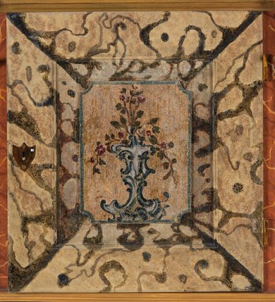 Zdjęcie nr 123: Umeblowanie zakrystii usytuowane jest wzdłuż ścian północnej, południowej i wschodniej pomieszczenia.  Na ścianie północnej, w części dolnej znajdują się trzy połączone ze sobą komody, każda o czterech szufladach, nakryte jednym blatem. W części górnej mieszczą się pięcioosiowe szafki z szufladami w cokole. Osie artykułowe są pilastrami hermowymi. Na osi środkowej szafka jest nieco wyższa i szersza z drzwiczkami dekorowanymi prostokątną, uszatą, oprofilowaną płyciną z malowanym przedstawieniem Chrystusa Eucharystycznego. Drzwiczki pozostałych szafek mają kształt stojących prostokątów i dekorowane są płycinami o wklęsłych narożach, zdobionymi gałązkami czerwonych róż, ułożonych w rokokowych wazonach. Ścianki zamknięte są niepełnym belkowaniem z gzymsem. W partii zwieńczenia osie artykułowane są cokolikami, na których ustawione są toczone, kuliste wazoniki. Pomiędzy nimi umieszczone są kartusze utworzone z ornamentu małżowinowo-chrząstkowego z malowanymi emblematami na owalnych medalionach, które ułożone są kolejno od lewej strony: 
1. Pionowo ustawiony miecz, ostrzem skierowany ku górze, połączony ze skrzyżowanymi berłem i dwoma kluczami, od których odchodzą fantazyjnie ułożone sznury w kolorze czerwonym. U góry napis na szarfie: „OBEDITE”.
2. W górnej części wyłaniająca się z chmur ręka trzymająca w dłoni węgielnicę i przymocowane do niej na łańcuszku tablice Dekalogu. Napis na szarfie: „OMNIA SVSTINET”.
3. Bóg Ojciec ukazany w półpostaci, lewą ręką opiera się na kuli ziemskiej, prawą czyni gest błogosławieństwa. 
4. Bujnie ulistnione, ciemnozielone drzewko spięte w dolnej części złotą formą w kształcie dwóch wywiniętych wolutek. Napis na szarfie: „GAVDET PATIENTIA DVRIS”. 
5. W górnej części obrazu z chmur wyłania się ręka, która zrzuca na ziemię iskrzący pocisk i dwa skrzyżowane pioruny, połączone parą białych skrzydeł. Napis „FORTIS VLTOR”.
 
Na ścianie środkowej, wschodniej znajduje się sarkofagowa mensa, powyżej parawanowa ścianka na profilowanym cokole, artykułowana pilastrami, pomiędzy którymi umieszczone są płyciny z kształcie leżących prostokątów z obrazami; ścianka zamknięta jest profilowanym gzymsem. W zwieńczeniu, na jej skrajach znajdują się owalne medaliony ujęte w kartusze z ornamentu małżowinowo-chrząstkowego. W medalionie po lewej stronie namalowane są litery alfa i omega na błękitnym tle oraz wstęga z napisem: „RENOVATUM A(NNO) D(OMINI) 1975”. Po prawej stronie analogiczny kartusz z literami w medalionie: „Ω / O / N” wpisane w formę krzyża, otoczonego niepełną aureolą; powyżej wstęga z napisem: „VIDENTEM AUDERE”. W płycinach obrazy przedstawiają świętych w ujęciu do pasa, zwróconych ku środkowi; od lewej:
1. Święty Demetriusz z włócznią opartą o prawy bark, ubrany w habit zakonu kanoników laterańskich od pokuty.
2. Święty Klet z aniołkiem, który trzyma w dłoni palmę męczeństwa i krzyż papieski. W prawym górnym narożu obrazu napis: „FAC HVIC SIGNO HONOREM”.
3. Święty Augustyn z gorejącym sercem na piersi i aniołkiem z łyżką i miseczką w dłoniach.
4. Święty ubrany w habit Marków, który trzyma w dłoni serce z krzyżem, podtrzymywane przez Chrystusa na obłokach – prawdopodobnie św. Cyriak, założyciel zakonu.
 
Na ścianie południowej znajduje się analogiczne umeblowanie, jak na ścianie północnej. W dolnej części dwie komody, a w miejscu trzeciej od wschodu szafka zdobiona dwiema uszatymi płycinami. Górna część mebla w przeciwieństwie do ściany północnej bez podwyższenia części środkowej. 
Na ścianie południowej:
1. Jasnobrązowa harfa na błękitnym tle i napis: „IN DOMINO”.
2. Ciemnobrązowy ptak i trzy podrywające się do lotu młode, w górnej części złote słońce i napis: „NON QUAE SVPER TERRAM.”
3. Po lewej stronie kompozycji wyłaniająca się z chmur ręka trzymająca skrzyżowane: miecz, czerwony krzyż i palmę. Napis: „NON ERVBESCO”.
4. W centrum przedstawienia krzak białej lilii o trzech rozgałęzieniach, w tle chmury w odcieniach koloru szaroniebieskiego. Napis na szarfie: „PER ARDVA DVLCIS”.
5. W lewej części kompozycji uskrzydlony jeleń, wspięty na tylnych nogach, po prawej stronie czarne i brązowe skały, w partii górnej otwarta korona, umieszczona pośrodku obłoku obwiedzionego biało-czerwonym pasem. Napis: „ET COMPREHENDATIS”.
 
W miejscu połączenia komód ścian północnej i południowej z dolną częścią konstrukcji na ścianie wschodniej znajdują się ukośnie ustawione, jednoskrzydłowe szafki o drzwiczkach dekorowanych prostokątną płyciną o wklęsłych narożach. Ścianki boczne części północnej i południowej zdobione są ukośną kratką. Powierzchnia szafek i komód pokryta jest polichromią imitującą marmur w kolorze beżowym, szarokremowym, różowym i rdzawym. Blaty malowane są farbą olejną w kolorze beżowym. Obramienia medalionów malowane w kolorze rdzawozłotym. Tło w większości medalionów w odcieniach błękitu, w górnych częściach majuskułowe napisy objaśniające przedstawienie, umieszczone w białych i półkoliście ułożonych szarfach. 