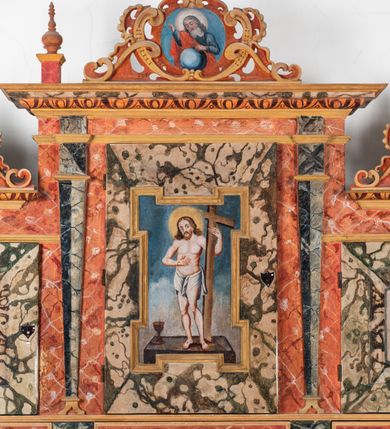 Zdjęcie nr 127: Umeblowanie zakrystii usytuowane jest wzdłuż ścian północnej, południowej i wschodniej pomieszczenia.  Na ścianie północnej, w części dolnej znajdują się trzy połączone ze sobą komody, każda o czterech szufladach, nakryte jednym blatem. W części górnej mieszczą się pięcioosiowe szafki z szufladami w cokole. Osie artykułowe są pilastrami hermowymi. Na osi środkowej szafka jest nieco wyższa i szersza z drzwiczkami dekorowanymi prostokątną, uszatą, oprofilowaną płyciną z malowanym przedstawieniem Chrystusa Eucharystycznego. Drzwiczki pozostałych szafek mają kształt stojących prostokątów i dekorowane są płycinami o wklęsłych narożach, zdobionymi gałązkami czerwonych róż, ułożonych w rokokowych wazonach. Ścianki zamknięte są niepełnym belkowaniem z gzymsem. W partii zwieńczenia osie artykułowane są cokolikami, na których ustawione są toczone, kuliste wazoniki. Pomiędzy nimi umieszczone są kartusze utworzone z ornamentu małżowinowo-chrząstkowego z malowanymi emblematami na owalnych medalionach, które ułożone są kolejno od lewej strony: 
1. Pionowo ustawiony miecz, ostrzem skierowany ku górze, połączony ze skrzyżowanymi berłem i dwoma kluczami, od których odchodzą fantazyjnie ułożone sznury w kolorze czerwonym. U góry napis na szarfie: „OBEDITE”.
2. W górnej części wyłaniająca się z chmur ręka trzymająca w dłoni węgielnicę i przymocowane do niej na łańcuszku tablice Dekalogu. Napis na szarfie: „OMNIA SVSTINET”.
3. Bóg Ojciec ukazany w półpostaci, lewą ręką opiera się na kuli ziemskiej, prawą czyni gest błogosławieństwa. 
4. Bujnie ulistnione, ciemnozielone drzewko spięte w dolnej części złotą formą w kształcie dwóch wywiniętych wolutek. Napis na szarfie: „GAVDET PATIENTIA DVRIS”. 
5. W górnej części obrazu z chmur wyłania się ręka, która zrzuca na ziemię iskrzący pocisk i dwa skrzyżowane pioruny, połączone parą białych skrzydeł. Napis „FORTIS VLTOR”.
 
Na ścianie środkowej, wschodniej znajduje się sarkofagowa mensa, powyżej parawanowa ścianka na profilowanym cokole, artykułowana pilastrami, pomiędzy którymi umieszczone są płyciny z kształcie leżących prostokątów z obrazami; ścianka zamknięta jest profilowanym gzymsem. W zwieńczeniu, na jej skrajach znajdują się owalne medaliony ujęte w kartusze z ornamentu małżowinowo-chrząstkowego. W medalionie po lewej stronie namalowane są litery alfa i omega na błękitnym tle oraz wstęga z napisem: „RENOVATUM A(NNO) D(OMINI) 1975”. Po prawej stronie analogiczny kartusz z literami w medalionie: „Ω / O / N” wpisane w formę krzyża, otoczonego niepełną aureolą; powyżej wstęga z napisem: „VIDENTEM AUDERE”. W płycinach obrazy przedstawiają świętych w ujęciu do pasa, zwróconych ku środkowi; od lewej:
1. Święty Demetriusz z włócznią opartą o prawy bark, ubrany w habit zakonu kanoników laterańskich od pokuty.
2. Święty Klet z aniołkiem, który trzyma w dłoni palmę męczeństwa i krzyż papieski. W prawym górnym narożu obrazu napis: „FAC HVIC SIGNO HONOREM”.
3. Święty Augustyn z gorejącym sercem na piersi i aniołkiem z łyżką i miseczką w dłoniach.
4. Święty ubrany w habit Marków, który trzyma w dłoni serce z krzyżem, podtrzymywane przez Chrystusa na obłokach – prawdopodobnie św. Cyriak, założyciel zakonu.
 
Na ścianie południowej znajduje się analogiczne umeblowanie, jak na ścianie północnej. W dolnej części dwie komody, a w miejscu trzeciej od wschodu szafka zdobiona dwiema uszatymi płycinami. Górna część mebla w przeciwieństwie do ściany północnej bez podwyższenia części środkowej. 
Na ścianie południowej:
1. Jasnobrązowa harfa na błękitnym tle i napis: „IN DOMINO”.
2. Ciemnobrązowy ptak i trzy podrywające się do lotu młode, w górnej części złote słońce i napis: „NON QUAE SVPER TERRAM.”
3. Po lewej stronie kompozycji wyłaniająca się z chmur ręka trzymająca skrzyżowane: miecz, czerwony krzyż i palmę. Napis: „NON ERVBESCO”.
4. W centrum przedstawienia krzak białej lilii o trzech rozgałęzieniach, w tle chmury w odcieniach koloru szaroniebieskiego. Napis na szarfie: „PER ARDVA DVLCIS”.
5. W lewej części kompozycji uskrzydlony jeleń, wspięty na tylnych nogach, po prawej stronie czarne i brązowe skały, w partii górnej otwarta korona, umieszczona pośrodku obłoku obwiedzionego biało-czerwonym pasem. Napis: „ET COMPREHENDATIS”.
 
W miejscu połączenia komód ścian północnej i południowej z dolną częścią konstrukcji na ścianie wschodniej znajdują się ukośnie ustawione, jednoskrzydłowe szafki o drzwiczkach dekorowanych prostokątną płyciną o wklęsłych narożach. Ścianki boczne części północnej i południowej zdobione są ukośną kratką. Powierzchnia szafek i komód pokryta jest polichromią imitującą marmur w kolorze beżowym, szarokremowym, różowym i rdzawym. Blaty malowane są farbą olejną w kolorze beżowym. Obramienia medalionów malowane w kolorze rdzawozłotym. Tło w większości medalionów w odcieniach błękitu, w górnych częściach majuskułowe napisy objaśniające przedstawienie, umieszczone w białych i półkoliście ułożonych szarfach. 