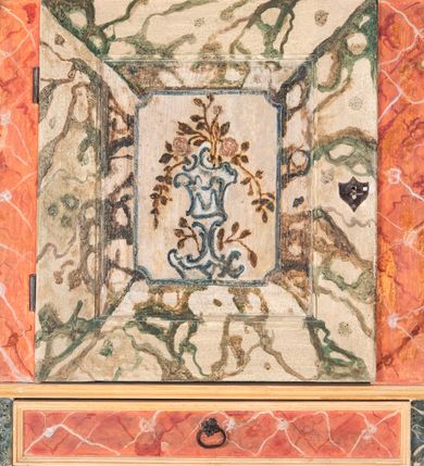 Zdjęcie nr 6: Umeblowanie zakrystii usytuowane jest wzdłuż ścian północnej, południowej i wschodniej pomieszczenia.  Na ścianie północnej, w części dolnej znajdują się trzy połączone ze sobą komody, każda o czterech szufladach, nakryte jednym blatem. W części górnej mieszczą się pięcioosiowe szafki z szufladami w cokole. Osie artykułowe są pilastrami hermowymi. Na osi środkowej szafka jest nieco wyższa i szersza z drzwiczkami dekorowanymi prostokątną, uszatą, oprofilowaną płyciną z malowanym przedstawieniem Chrystusa Eucharystycznego. Drzwiczki pozostałych szafek mają kształt stojących prostokątów i dekorowane są płycinami o wklęsłych narożach, zdobionymi gałązkami czerwonych róż, ułożonych w rokokowych wazonach. Ścianki zamknięte są niepełnym belkowaniem z gzymsem. W partii zwieńczenia osie artykułowane są cokolikami, na których ustawione są toczone, kuliste wazoniki. Pomiędzy nimi umieszczone są kartusze utworzone z ornamentu małżowinowo-chrząstkowego z malowanymi emblematami na owalnych medalionach, które ułożone są kolejno od lewej strony: 
1. Pionowo ustawiony miecz, ostrzem skierowany ku górze, połączony ze skrzyżowanymi berłem i dwoma kluczami, od których odchodzą fantazyjnie ułożone sznury w kolorze czerwonym. U góry napis na szarfie: „OBEDITE”.
2. W górnej części wyłaniająca się z chmur ręka trzymająca w dłoni węgielnicę i przymocowane do niej na łańcuszku tablice Dekalogu. Napis na szarfie: „OMNIA SVSTINET”.
3. Bóg Ojciec ukazany w półpostaci, lewą ręką opiera się na kuli ziemskiej, prawą czyni gest błogosławieństwa. 
4. Bujnie ulistnione, ciemnozielone drzewko spięte w dolnej części złotą formą w kształcie dwóch wywiniętych wolutek. Napis na szarfie: „GAVDET PATIENTIA DVRIS”. 
5. W górnej części obrazu z chmur wyłania się ręka, która zrzuca na ziemię iskrzący pocisk i dwa skrzyżowane pioruny, połączone parą białych skrzydeł. Napis „FORTIS VLTOR”.
 
Na ścianie środkowej, wschodniej znajduje się sarkofagowa mensa, powyżej parawanowa ścianka na profilowanym cokole, artykułowana pilastrami, pomiędzy którymi umieszczone są płyciny z kształcie leżących prostokątów z obrazami; ścianka zamknięta jest profilowanym gzymsem. W zwieńczeniu, na jej skrajach znajdują się owalne medaliony ujęte w kartusze z ornamentu małżowinowo-chrząstkowego. W medalionie po lewej stronie namalowane są litery alfa i omega na błękitnym tle oraz wstęga z napisem: „RENOVATUM A(NNO) D(OMINI) 1975”. Po prawej stronie analogiczny kartusz z literami w medalionie: „Ω / O / N” wpisane w formę krzyża, otoczonego niepełną aureolą; powyżej wstęga z napisem: „VIDENTEM AUDERE”. W płycinach obrazy przedstawiają świętych w ujęciu do pasa, zwróconych ku środkowi; od lewej:
1. Święty Demetriusz z włócznią opartą o prawy bark, ubrany w habit zakonu kanoników laterańskich od pokuty.
2. Święty Klet z aniołkiem, który trzyma w dłoni palmę męczeństwa i krzyż papieski. W prawym górnym narożu obrazu napis: „FAC HVIC SIGNO HONOREM”.
3. Święty Augustyn z gorejącym sercem na piersi i aniołkiem z łyżką i miseczką w dłoniach.
4. Święty ubrany w habit Marków, który trzyma w dłoni serce z krzyżem, podtrzymywane przez Chrystusa na obłokach – prawdopodobnie św. Cyriak, założyciel zakonu.
 
Na ścianie południowej znajduje się analogiczne umeblowanie, jak na ścianie północnej. W dolnej części dwie komody, a w miejscu trzeciej od wschodu szafka zdobiona dwiema uszatymi płycinami. Górna część mebla w przeciwieństwie do ściany północnej bez podwyższenia części środkowej. 
Na ścianie południowej:
1. Jasnobrązowa harfa na błękitnym tle i napis: „IN DOMINO”.
2. Ciemnobrązowy ptak i trzy podrywające się do lotu młode, w górnej części złote słońce i napis: „NON QUAE SVPER TERRAM.”
3. Po lewej stronie kompozycji wyłaniająca się z chmur ręka trzymająca skrzyżowane: miecz, czerwony krzyż i palmę. Napis: „NON ERVBESCO”.
4. W centrum przedstawienia krzak białej lilii o trzech rozgałęzieniach, w tle chmury w odcieniach koloru szaroniebieskiego. Napis na szarfie: „PER ARDVA DVLCIS”.
5. W lewej części kompozycji uskrzydlony jeleń, wspięty na tylnych nogach, po prawej stronie czarne i brązowe skały, w partii górnej otwarta korona, umieszczona pośrodku obłoku obwiedzionego biało-czerwonym pasem. Napis: „ET COMPREHENDATIS”.
 
W miejscu połączenia komód ścian północnej i południowej z dolną częścią konstrukcji na ścianie wschodniej znajdują się ukośnie ustawione, jednoskrzydłowe szafki o drzwiczkach dekorowanych prostokątną płyciną o wklęsłych narożach. Ścianki boczne części północnej i południowej zdobione są ukośną kratką. Powierzchnia szafek i komód pokryta jest polichromią imitującą marmur w kolorze beżowym, szarokremowym, różowym i rdzawym. Blaty malowane są farbą olejną w kolorze beżowym. Obramienia medalionów malowane w kolorze rdzawozłotym. Tło w większości medalionów w odcieniach błękitu, w górnych częściach majuskułowe napisy objaśniające przedstawienie, umieszczone w białych i półkoliście ułożonych szarfach. 