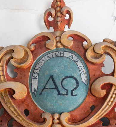 Zdjęcie nr 9: Umeblowanie zakrystii usytuowane jest wzdłuż ścian północnej, południowej i wschodniej pomieszczenia.  Na ścianie północnej, w części dolnej znajdują się trzy połączone ze sobą komody, każda o czterech szufladach, nakryte jednym blatem. W części górnej mieszczą się pięcioosiowe szafki z szufladami w cokole. Osie artykułowe są pilastrami hermowymi. Na osi środkowej szafka jest nieco wyższa i szersza z drzwiczkami dekorowanymi prostokątną, uszatą, oprofilowaną płyciną z malowanym przedstawieniem Chrystusa Eucharystycznego. Drzwiczki pozostałych szafek mają kształt stojących prostokątów i dekorowane są płycinami o wklęsłych narożach, zdobionymi gałązkami czerwonych róż, ułożonych w rokokowych wazonach. Ścianki zamknięte są niepełnym belkowaniem z gzymsem. W partii zwieńczenia osie artykułowane są cokolikami, na których ustawione są toczone, kuliste wazoniki. Pomiędzy nimi umieszczone są kartusze utworzone z ornamentu małżowinowo-chrząstkowego z malowanymi emblematami na owalnych medalionach, które ułożone są kolejno od lewej strony: 
1. Pionowo ustawiony miecz, ostrzem skierowany ku górze, połączony ze skrzyżowanymi berłem i dwoma kluczami, od których odchodzą fantazyjnie ułożone sznury w kolorze czerwonym. U góry napis na szarfie: „OBEDITE”.
2. W górnej części wyłaniająca się z chmur ręka trzymająca w dłoni węgielnicę i przymocowane do niej na łańcuszku tablice Dekalogu. Napis na szarfie: „OMNIA SVSTINET”.
3. Bóg Ojciec ukazany w półpostaci, lewą ręką opiera się na kuli ziemskiej, prawą czyni gest błogosławieństwa. 
4. Bujnie ulistnione, ciemnozielone drzewko spięte w dolnej części złotą formą w kształcie dwóch wywiniętych wolutek. Napis na szarfie: „GAVDET PATIENTIA DVRIS”. 
5. W górnej części obrazu z chmur wyłania się ręka, która zrzuca na ziemię iskrzący pocisk i dwa skrzyżowane pioruny, połączone parą białych skrzydeł. Napis „FORTIS VLTOR”.
 
Na ścianie środkowej, wschodniej znajduje się sarkofagowa mensa, powyżej parawanowa ścianka na profilowanym cokole, artykułowana pilastrami, pomiędzy którymi umieszczone są płyciny z kształcie leżących prostokątów z obrazami; ścianka zamknięta jest profilowanym gzymsem. W zwieńczeniu, na jej skrajach znajdują się owalne medaliony ujęte w kartusze z ornamentu małżowinowo-chrząstkowego. W medalionie po lewej stronie namalowane są litery alfa i omega na błękitnym tle oraz wstęga z napisem: „RENOVATUM A(NNO) D(OMINI) 1975”. Po prawej stronie analogiczny kartusz z literami w medalionie: „Ω / O / N” wpisane w formę krzyża, otoczonego niepełną aureolą; powyżej wstęga z napisem: „VIDENTEM AUDERE”. W płycinach obrazy przedstawiają świętych w ujęciu do pasa, zwróconych ku środkowi; od lewej:
1. Święty Demetriusz z włócznią opartą o prawy bark, ubrany w habit zakonu kanoników laterańskich od pokuty.
2. Święty Klet z aniołkiem, który trzyma w dłoni palmę męczeństwa i krzyż papieski. W prawym górnym narożu obrazu napis: „FAC HVIC SIGNO HONOREM”.
3. Święty Augustyn z gorejącym sercem na piersi i aniołkiem z łyżką i miseczką w dłoniach.
4. Święty ubrany w habit Marków, który trzyma w dłoni serce z krzyżem, podtrzymywane przez Chrystusa na obłokach – prawdopodobnie św. Cyriak, założyciel zakonu.
 
Na ścianie południowej znajduje się analogiczne umeblowanie, jak na ścianie północnej. W dolnej części dwie komody, a w miejscu trzeciej od wschodu szafka zdobiona dwiema uszatymi płycinami. Górna część mebla w przeciwieństwie do ściany północnej bez podwyższenia części środkowej. 
Na ścianie południowej:
1. Jasnobrązowa harfa na błękitnym tle i napis: „IN DOMINO”.
2. Ciemnobrązowy ptak i trzy podrywające się do lotu młode, w górnej części złote słońce i napis: „NON QUAE SVPER TERRAM.”
3. Po lewej stronie kompozycji wyłaniająca się z chmur ręka trzymająca skrzyżowane: miecz, czerwony krzyż i palmę. Napis: „NON ERVBESCO”.
4. W centrum przedstawienia krzak białej lilii o trzech rozgałęzieniach, w tle chmury w odcieniach koloru szaroniebieskiego. Napis na szarfie: „PER ARDVA DVLCIS”.
5. W lewej części kompozycji uskrzydlony jeleń, wspięty na tylnych nogach, po prawej stronie czarne i brązowe skały, w partii górnej otwarta korona, umieszczona pośrodku obłoku obwiedzionego biało-czerwonym pasem. Napis: „ET COMPREHENDATIS”.
 
W miejscu połączenia komód ścian północnej i południowej z dolną częścią konstrukcji na ścianie wschodniej znajdują się ukośnie ustawione, jednoskrzydłowe szafki o drzwiczkach dekorowanych prostokątną płyciną o wklęsłych narożach. Ścianki boczne części północnej i południowej zdobione są ukośną kratką. Powierzchnia szafek i komód pokryta jest polichromią imitującą marmur w kolorze beżowym, szarokremowym, różowym i rdzawym. Blaty malowane są farbą olejną w kolorze beżowym. Obramienia medalionów malowane w kolorze rdzawozłotym. Tło w większości medalionów w odcieniach błękitu, w górnych częściach majuskułowe napisy objaśniające przedstawienie, umieszczone w białych i półkoliście ułożonych szarfach. 