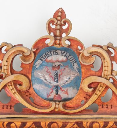 Zdjęcie nr 12: Umeblowanie zakrystii usytuowane jest wzdłuż ścian północnej, południowej i wschodniej pomieszczenia.  Na ścianie północnej, w części dolnej znajdują się trzy połączone ze sobą komody, każda o czterech szufladach, nakryte jednym blatem. W części górnej mieszczą się pięcioosiowe szafki z szufladami w cokole. Osie artykułowe są pilastrami hermowymi. Na osi środkowej szafka jest nieco wyższa i szersza z drzwiczkami dekorowanymi prostokątną, uszatą, oprofilowaną płyciną z malowanym przedstawieniem Chrystusa Eucharystycznego. Drzwiczki pozostałych szafek mają kształt stojących prostokątów i dekorowane są płycinami o wklęsłych narożach, zdobionymi gałązkami czerwonych róż, ułożonych w rokokowych wazonach. Ścianki zamknięte są niepełnym belkowaniem z gzymsem. W partii zwieńczenia osie artykułowane są cokolikami, na których ustawione są toczone, kuliste wazoniki. Pomiędzy nimi umieszczone są kartusze utworzone z ornamentu małżowinowo-chrząstkowego z malowanymi emblematami na owalnych medalionach, które ułożone są kolejno od lewej strony: 
1. Pionowo ustawiony miecz, ostrzem skierowany ku górze, połączony ze skrzyżowanymi berłem i dwoma kluczami, od których odchodzą fantazyjnie ułożone sznury w kolorze czerwonym. U góry napis na szarfie: „OBEDITE”.
2. W górnej części wyłaniająca się z chmur ręka trzymająca w dłoni węgielnicę i przymocowane do niej na łańcuszku tablice Dekalogu. Napis na szarfie: „OMNIA SVSTINET”.
3. Bóg Ojciec ukazany w półpostaci, lewą ręką opiera się na kuli ziemskiej, prawą czyni gest błogosławieństwa. 
4. Bujnie ulistnione, ciemnozielone drzewko spięte w dolnej części złotą formą w kształcie dwóch wywiniętych wolutek. Napis na szarfie: „GAVDET PATIENTIA DVRIS”. 
5. W górnej części obrazu z chmur wyłania się ręka, która zrzuca na ziemię iskrzący pocisk i dwa skrzyżowane pioruny, połączone parą białych skrzydeł. Napis „FORTIS VLTOR”.
 
Na ścianie środkowej, wschodniej znajduje się sarkofagowa mensa, powyżej parawanowa ścianka na profilowanym cokole, artykułowana pilastrami, pomiędzy którymi umieszczone są płyciny z kształcie leżących prostokątów z obrazami; ścianka zamknięta jest profilowanym gzymsem. W zwieńczeniu, na jej skrajach znajdują się owalne medaliony ujęte w kartusze z ornamentu małżowinowo-chrząstkowego. W medalionie po lewej stronie namalowane są litery alfa i omega na błękitnym tle oraz wstęga z napisem: „RENOVATUM A(NNO) D(OMINI) 1975”. Po prawej stronie analogiczny kartusz z literami w medalionie: „Ω / O / N” wpisane w formę krzyża, otoczonego niepełną aureolą; powyżej wstęga z napisem: „VIDENTEM AUDERE”. W płycinach obrazy przedstawiają świętych w ujęciu do pasa, zwróconych ku środkowi; od lewej:
1. Święty Demetriusz z włócznią opartą o prawy bark, ubrany w habit zakonu kanoników laterańskich od pokuty.
2. Święty Klet z aniołkiem, który trzyma w dłoni palmę męczeństwa i krzyż papieski. W prawym górnym narożu obrazu napis: „FAC HVIC SIGNO HONOREM”.
3. Święty Augustyn z gorejącym sercem na piersi i aniołkiem z łyżką i miseczką w dłoniach.
4. Święty ubrany w habit Marków, który trzyma w dłoni serce z krzyżem, podtrzymywane przez Chrystusa na obłokach – prawdopodobnie św. Cyriak, założyciel zakonu.
 
Na ścianie południowej znajduje się analogiczne umeblowanie, jak na ścianie północnej. W dolnej części dwie komody, a w miejscu trzeciej od wschodu szafka zdobiona dwiema uszatymi płycinami. Górna część mebla w przeciwieństwie do ściany północnej bez podwyższenia części środkowej. 
Na ścianie południowej:
1. Jasnobrązowa harfa na błękitnym tle i napis: „IN DOMINO”.
2. Ciemnobrązowy ptak i trzy podrywające się do lotu młode, w górnej części złote słońce i napis: „NON QUAE SVPER TERRAM.”
3. Po lewej stronie kompozycji wyłaniająca się z chmur ręka trzymająca skrzyżowane: miecz, czerwony krzyż i palmę. Napis: „NON ERVBESCO”.
4. W centrum przedstawienia krzak białej lilii o trzech rozgałęzieniach, w tle chmury w odcieniach koloru szaroniebieskiego. Napis na szarfie: „PER ARDVA DVLCIS”.
5. W lewej części kompozycji uskrzydlony jeleń, wspięty na tylnych nogach, po prawej stronie czarne i brązowe skały, w partii górnej otwarta korona, umieszczona pośrodku obłoku obwiedzionego biało-czerwonym pasem. Napis: „ET COMPREHENDATIS”.
 
W miejscu połączenia komód ścian północnej i południowej z dolną częścią konstrukcji na ścianie wschodniej znajdują się ukośnie ustawione, jednoskrzydłowe szafki o drzwiczkach dekorowanych prostokątną płyciną o wklęsłych narożach. Ścianki boczne części północnej i południowej zdobione są ukośną kratką. Powierzchnia szafek i komód pokryta jest polichromią imitującą marmur w kolorze beżowym, szarokremowym, różowym i rdzawym. Blaty malowane są farbą olejną w kolorze beżowym. Obramienia medalionów malowane w kolorze rdzawozłotym. Tło w większości medalionów w odcieniach błękitu, w górnych częściach majuskułowe napisy objaśniające przedstawienie, umieszczone w białych i półkoliście ułożonych szarfach. 