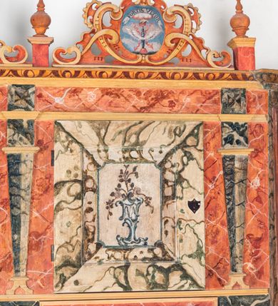 Zdjęcie nr 18: Umeblowanie zakrystii usytuowane jest wzdłuż ścian północnej, południowej i wschodniej pomieszczenia.  Na ścianie północnej, w części dolnej znajdują się trzy połączone ze sobą komody, każda o czterech szufladach, nakryte jednym blatem. W części górnej mieszczą się pięcioosiowe szafki z szufladami w cokole. Osie artykułowe są pilastrami hermowymi. Na osi środkowej szafka jest nieco wyższa i szersza z drzwiczkami dekorowanymi prostokątną, uszatą, oprofilowaną płyciną z malowanym przedstawieniem Chrystusa Eucharystycznego. Drzwiczki pozostałych szafek mają kształt stojących prostokątów i dekorowane są płycinami o wklęsłych narożach, zdobionymi gałązkami czerwonych róż, ułożonych w rokokowych wazonach. Ścianki zamknięte są niepełnym belkowaniem z gzymsem. W partii zwieńczenia osie artykułowane są cokolikami, na których ustawione są toczone, kuliste wazoniki. Pomiędzy nimi umieszczone są kartusze utworzone z ornamentu małżowinowo-chrząstkowego z malowanymi emblematami na owalnych medalionach, które ułożone są kolejno od lewej strony: 
1. Pionowo ustawiony miecz, ostrzem skierowany ku górze, połączony ze skrzyżowanymi berłem i dwoma kluczami, od których odchodzą fantazyjnie ułożone sznury w kolorze czerwonym. U góry napis na szarfie: „OBEDITE”.
2. W górnej części wyłaniająca się z chmur ręka trzymająca w dłoni węgielnicę i przymocowane do niej na łańcuszku tablice Dekalogu. Napis na szarfie: „OMNIA SVSTINET”.
3. Bóg Ojciec ukazany w półpostaci, lewą ręką opiera się na kuli ziemskiej, prawą czyni gest błogosławieństwa. 
4. Bujnie ulistnione, ciemnozielone drzewko spięte w dolnej części złotą formą w kształcie dwóch wywiniętych wolutek. Napis na szarfie: „GAVDET PATIENTIA DVRIS”. 
5. W górnej części obrazu z chmur wyłania się ręka, która zrzuca na ziemię iskrzący pocisk i dwa skrzyżowane pioruny, połączone parą białych skrzydeł. Napis „FORTIS VLTOR”.
 
Na ścianie środkowej, wschodniej znajduje się sarkofagowa mensa, powyżej parawanowa ścianka na profilowanym cokole, artykułowana pilastrami, pomiędzy którymi umieszczone są płyciny z kształcie leżących prostokątów z obrazami; ścianka zamknięta jest profilowanym gzymsem. W zwieńczeniu, na jej skrajach znajdują się owalne medaliony ujęte w kartusze z ornamentu małżowinowo-chrząstkowego. W medalionie po lewej stronie namalowane są litery alfa i omega na błękitnym tle oraz wstęga z napisem: „RENOVATUM A(NNO) D(OMINI) 1975”. Po prawej stronie analogiczny kartusz z literami w medalionie: „Ω / O / N” wpisane w formę krzyża, otoczonego niepełną aureolą; powyżej wstęga z napisem: „VIDENTEM AUDERE”. W płycinach obrazy przedstawiają świętych w ujęciu do pasa, zwróconych ku środkowi; od lewej:
1. Święty Demetriusz z włócznią opartą o prawy bark, ubrany w habit zakonu kanoników laterańskich od pokuty.
2. Święty Klet z aniołkiem, który trzyma w dłoni palmę męczeństwa i krzyż papieski. W prawym górnym narożu obrazu napis: „FAC HVIC SIGNO HONOREM”.
3. Święty Augustyn z gorejącym sercem na piersi i aniołkiem z łyżką i miseczką w dłoniach.
4. Święty ubrany w habit Marków, który trzyma w dłoni serce z krzyżem, podtrzymywane przez Chrystusa na obłokach – prawdopodobnie św. Cyriak, założyciel zakonu.
 
Na ścianie południowej znajduje się analogiczne umeblowanie, jak na ścianie północnej. W dolnej części dwie komody, a w miejscu trzeciej od wschodu szafka zdobiona dwiema uszatymi płycinami. Górna część mebla w przeciwieństwie do ściany północnej bez podwyższenia części środkowej. 
Na ścianie południowej:
1. Jasnobrązowa harfa na błękitnym tle i napis: „IN DOMINO”.
2. Ciemnobrązowy ptak i trzy podrywające się do lotu młode, w górnej części złote słońce i napis: „NON QUAE SVPER TERRAM.”
3. Po lewej stronie kompozycji wyłaniająca się z chmur ręka trzymająca skrzyżowane: miecz, czerwony krzyż i palmę. Napis: „NON ERVBESCO”.
4. W centrum przedstawienia krzak białej lilii o trzech rozgałęzieniach, w tle chmury w odcieniach koloru szaroniebieskiego. Napis na szarfie: „PER ARDVA DVLCIS”.
5. W lewej części kompozycji uskrzydlony jeleń, wspięty na tylnych nogach, po prawej stronie czarne i brązowe skały, w partii górnej otwarta korona, umieszczona pośrodku obłoku obwiedzionego biało-czerwonym pasem. Napis: „ET COMPREHENDATIS”.
 
W miejscu połączenia komód ścian północnej i południowej z dolną częścią konstrukcji na ścianie wschodniej znajdują się ukośnie ustawione, jednoskrzydłowe szafki o drzwiczkach dekorowanych prostokątną płyciną o wklęsłych narożach. Ścianki boczne części północnej i południowej zdobione są ukośną kratką. Powierzchnia szafek i komód pokryta jest polichromią imitującą marmur w kolorze beżowym, szarokremowym, różowym i rdzawym. Blaty malowane są farbą olejną w kolorze beżowym. Obramienia medalionów malowane w kolorze rdzawozłotym. Tło w większości medalionów w odcieniach błękitu, w górnych częściach majuskułowe napisy objaśniające przedstawienie, umieszczone w białych i półkoliście ułożonych szarfach. 