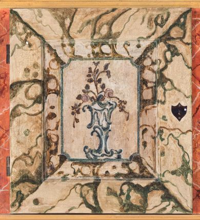 Zdjęcie nr 15: Umeblowanie zakrystii usytuowane jest wzdłuż ścian północnej, południowej i wschodniej pomieszczenia.  Na ścianie północnej, w części dolnej znajdują się trzy połączone ze sobą komody, każda o czterech szufladach, nakryte jednym blatem. W części górnej mieszczą się pięcioosiowe szafki z szufladami w cokole. Osie artykułowe są pilastrami hermowymi. Na osi środkowej szafka jest nieco wyższa i szersza z drzwiczkami dekorowanymi prostokątną, uszatą, oprofilowaną płyciną z malowanym przedstawieniem Chrystusa Eucharystycznego. Drzwiczki pozostałych szafek mają kształt stojących prostokątów i dekorowane są płycinami o wklęsłych narożach, zdobionymi gałązkami czerwonych róż, ułożonych w rokokowych wazonach. Ścianki zamknięte są niepełnym belkowaniem z gzymsem. W partii zwieńczenia osie artykułowane są cokolikami, na których ustawione są toczone, kuliste wazoniki. Pomiędzy nimi umieszczone są kartusze utworzone z ornamentu małżowinowo-chrząstkowego z malowanymi emblematami na owalnych medalionach, które ułożone są kolejno od lewej strony: 
1. Pionowo ustawiony miecz, ostrzem skierowany ku górze, połączony ze skrzyżowanymi berłem i dwoma kluczami, od których odchodzą fantazyjnie ułożone sznury w kolorze czerwonym. U góry napis na szarfie: „OBEDITE”.
2. W górnej części wyłaniająca się z chmur ręka trzymająca w dłoni węgielnicę i przymocowane do niej na łańcuszku tablice Dekalogu. Napis na szarfie: „OMNIA SVSTINET”.
3. Bóg Ojciec ukazany w półpostaci, lewą ręką opiera się na kuli ziemskiej, prawą czyni gest błogosławieństwa. 
4. Bujnie ulistnione, ciemnozielone drzewko spięte w dolnej części złotą formą w kształcie dwóch wywiniętych wolutek. Napis na szarfie: „GAVDET PATIENTIA DVRIS”. 
5. W górnej części obrazu z chmur wyłania się ręka, która zrzuca na ziemię iskrzący pocisk i dwa skrzyżowane pioruny, połączone parą białych skrzydeł. Napis „FORTIS VLTOR”.
 
Na ścianie środkowej, wschodniej znajduje się sarkofagowa mensa, powyżej parawanowa ścianka na profilowanym cokole, artykułowana pilastrami, pomiędzy którymi umieszczone są płyciny z kształcie leżących prostokątów z obrazami; ścianka zamknięta jest profilowanym gzymsem. W zwieńczeniu, na jej skrajach znajdują się owalne medaliony ujęte w kartusze z ornamentu małżowinowo-chrząstkowego. W medalionie po lewej stronie namalowane są litery alfa i omega na błękitnym tle oraz wstęga z napisem: „RENOVATUM A(NNO) D(OMINI) 1975”. Po prawej stronie analogiczny kartusz z literami w medalionie: „Ω / O / N” wpisane w formę krzyża, otoczonego niepełną aureolą; powyżej wstęga z napisem: „VIDENTEM AUDERE”. W płycinach obrazy przedstawiają świętych w ujęciu do pasa, zwróconych ku środkowi; od lewej:
1. Święty Demetriusz z włócznią opartą o prawy bark, ubrany w habit zakonu kanoników laterańskich od pokuty.
2. Święty Klet z aniołkiem, który trzyma w dłoni palmę męczeństwa i krzyż papieski. W prawym górnym narożu obrazu napis: „FAC HVIC SIGNO HONOREM”.
3. Święty Augustyn z gorejącym sercem na piersi i aniołkiem z łyżką i miseczką w dłoniach.
4. Święty ubrany w habit Marków, który trzyma w dłoni serce z krzyżem, podtrzymywane przez Chrystusa na obłokach – prawdopodobnie św. Cyriak, założyciel zakonu.
 
Na ścianie południowej znajduje się analogiczne umeblowanie, jak na ścianie północnej. W dolnej części dwie komody, a w miejscu trzeciej od wschodu szafka zdobiona dwiema uszatymi płycinami. Górna część mebla w przeciwieństwie do ściany północnej bez podwyższenia części środkowej. 
Na ścianie południowej:
1. Jasnobrązowa harfa na błękitnym tle i napis: „IN DOMINO”.
2. Ciemnobrązowy ptak i trzy podrywające się do lotu młode, w górnej części złote słońce i napis: „NON QUAE SVPER TERRAM.”
3. Po lewej stronie kompozycji wyłaniająca się z chmur ręka trzymająca skrzyżowane: miecz, czerwony krzyż i palmę. Napis: „NON ERVBESCO”.
4. W centrum przedstawienia krzak białej lilii o trzech rozgałęzieniach, w tle chmury w odcieniach koloru szaroniebieskiego. Napis na szarfie: „PER ARDVA DVLCIS”.
5. W lewej części kompozycji uskrzydlony jeleń, wspięty na tylnych nogach, po prawej stronie czarne i brązowe skały, w partii górnej otwarta korona, umieszczona pośrodku obłoku obwiedzionego biało-czerwonym pasem. Napis: „ET COMPREHENDATIS”.
 
W miejscu połączenia komód ścian północnej i południowej z dolną częścią konstrukcji na ścianie wschodniej znajdują się ukośnie ustawione, jednoskrzydłowe szafki o drzwiczkach dekorowanych prostokątną płyciną o wklęsłych narożach. Ścianki boczne części północnej i południowej zdobione są ukośną kratką. Powierzchnia szafek i komód pokryta jest polichromią imitującą marmur w kolorze beżowym, szarokremowym, różowym i rdzawym. Blaty malowane są farbą olejną w kolorze beżowym. Obramienia medalionów malowane w kolorze rdzawozłotym. Tło w większości medalionów w odcieniach błękitu, w górnych częściach majuskułowe napisy objaśniające przedstawienie, umieszczone w białych i półkoliście ułożonych szarfach. 