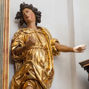 Zdjęcie nr 1: Rzeźba niemal pełnoplastyczna, ścięta. Stoi na konsoli małżowinowo chrząstkowej w lekkim kontrapoście z ciężarem ciała opartym na lewej nodze, ukazana jest frontalnie z wysuniętymi do przodu rękami ugiętymi w łokciach na wysokości pasa i głową przechyloną w prawo. Owalna, wydłużona twarz o pełnych policzkach, długim nosie, wąskich ustach i szeroko otwartych oczach, włosy krótkie faliste, rozwiane, zakrywające uszy. Rzeźba ubrana jest w tunikę z podwiniętymi rękawami, przepasaną na biodrze, odsłaniającą prawe udo i część lewej łydki oraz zarzucony na lewe ramię płaszcz z połą zarzuconą na prawe udo. Szaty modelowane ostrymi krawędziami, z podwiniętą dolną częścią płaszcza.