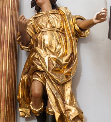 Zdjęcie nr 2: Rzeźba niemal pełnoplastyczna, ścięta. Stoi na konsoli małżowinowo chrząstkowej w lekkim kontrapoście z ciężarem ciała opartym na lewej nodze, ukazana jest frontalnie z wysuniętymi do przodu rękami ugiętymi w łokciach na wysokości pasa i głową przechyloną w prawo. Owalna, wydłużona twarz o pełnych policzkach, długim nosie, wąskich ustach i szeroko otwartych oczach, włosy krótkie faliste, rozwiane, zakrywające uszy. Rzeźba ubrana jest w tunikę z podwiniętymi rękawami, przepasaną na biodrze, odsłaniającą prawe udo i część lewej łydki oraz zarzucony na lewe ramię płaszcz z połą zarzuconą na prawe udo. Szaty modelowane ostrymi krawędziami, z podwiniętą dolną częścią płaszcza.