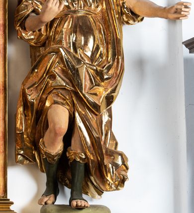 Zdjęcie nr 3: Rzeźba niemal pełnoplastyczna, ścięta. Stoi na konsoli małżowinowo chrząstkowej w lekkim kontrapoście z ciężarem ciała opartym na lewej nodze, ukazana jest frontalnie z wysuniętymi do przodu rękami ugiętymi w łokciach na wysokości pasa i głową przechyloną w prawo. Owalna, wydłużona twarz o pełnych policzkach, długim nosie, wąskich ustach i szeroko otwartych oczach, włosy krótkie faliste, rozwiane, zakrywające uszy. Rzeźba ubrana jest w tunikę z podwiniętymi rękawami, przepasaną na biodrze, odsłaniającą prawe udo i część lewej łydki oraz zarzucony na lewe ramię płaszcz z połą zarzuconą na prawe udo. Szaty modelowane ostrymi krawędziami, z podwiniętą dolną częścią płaszcza.