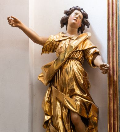 Zdjęcie nr 1: Forma niemal pełnoplastyczna i ścięta. Rzeźba stoi na konsoli małżowinowo chrząstkowej w lekkim kontrapoście z ciężarem ciała opartym na prawej nodze, ukazana jest frontalnie z wysuniętymi do przodu rękami, prawa uniesiona na wysokości głowy i znacznie odsunięta od tułowia, lewa lekko ugięta w łokciu na wysokości pasa.  Głowa przechylona w lewo. Okrągła twarz o pełnych policzkach i małym podbródku, długim nosie, wąskich, drobnych ustach i  szeroko otwartych oczach, włosy krótkie faliste, rozwiane, nieznacznie odkrywające uszy. Rzeźba ubrana jest w tunikę z podwiniętymi rękawami, przepasaną na biodrze, odsłaniającą lewe udo oraz w zarzucony na lewe ramię płaszcz z połą zarzuconą na prawe udo. Szaty modelowane ostrymi krawędziami, z podwiniętą dolną częścią płaszcza.