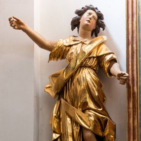 Zdjęcie nr 1: Forma niemal pełnoplastyczna i ścięta. Rzeźba stoi na konsoli małżowinowo chrząstkowej w lekkim kontrapoście z ciężarem ciała opartym na prawej nodze, ukazana jest frontalnie z wysuniętymi do przodu rękami, prawa uniesiona na wysokości głowy i znacznie odsunięta od tułowia, lewa lekko ugięta w łokciu na wysokości pasa.  Głowa przechylona w lewo. Okrągła twarz o pełnych policzkach i małym podbródku, długim nosie, wąskich, drobnych ustach i  szeroko otwartych oczach, włosy krótkie faliste, rozwiane, nieznacznie odkrywające uszy. Rzeźba ubrana jest w tunikę z podwiniętymi rękawami, przepasaną na biodrze, odsłaniającą lewe udo oraz w zarzucony na lewe ramię płaszcz z połą zarzuconą na prawe udo. Szaty modelowane ostrymi krawędziami, z podwiniętą dolną częścią płaszcza.