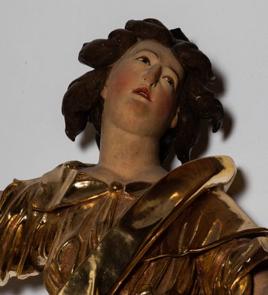 Zdjęcie nr 4: Forma niemal pełnoplastyczna i ścięta. Rzeźba stoi na konsoli małżowinowo chrząstkowej w lekkim kontrapoście z ciężarem ciała opartym na prawej nodze, ukazana jest frontalnie z wysuniętymi do przodu rękami, prawa uniesiona na wysokości głowy i znacznie odsunięta od tułowia, lewa lekko ugięta w łokciu na wysokości pasa.  Głowa przechylona w lewo. Okrągła twarz o pełnych policzkach i małym podbródku, długim nosie, wąskich, drobnych ustach i  szeroko otwartych oczach, włosy krótkie faliste, rozwiane, nieznacznie odkrywające uszy. Rzeźba ubrana jest w tunikę z podwiniętymi rękawami, przepasaną na biodrze, odsłaniającą lewe udo oraz w zarzucony na lewe ramię płaszcz z połą zarzuconą na prawe udo. Szaty modelowane ostrymi krawędziami, z podwiniętą dolną częścią płaszcza.