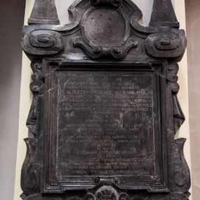 Zdjęcie nr 1: Tablica w kształcie stojącego prostokąta w profilowanej ramie z uskokami na narożach, wsparta na dwóch spłaszczonych wolutach i kartuszu z wyobrażeniem biretu na księdze z syglami &quot;A&quot; i &quot;W&quot; (Aalbertus Walkowicz). Tablicę ujmują spływy wolutowe, podwieszone draperie i wolutki, a wieńczy owalne pole flankowane spłaszczonymi ślimacznicami przechodzącymi w zawiniętą do środka wolutę. Na ślimacznicach osadzone niskie obeliski, a na wolucie krzyż o ramionach zamkniętych trójbocznie z promieniami. W polu Inskrypcja: &quot;D[EO] O[PTIMO] M[AXIMO] / QVI VIXIT BENE / MORTVVS BEATUS / NOX EIVS / LVX ANIMI EST / M(GISTER) A(DA)LBERTUS WAŁKOWIC VSTIENSIS PHI(LOSOPHI)AE et IV/RIS VTRIUSQUE DOCTOR AECCL(ESI)AE COL[E]G[IA]TAE SS. O(M)NIUM CRAC(OVIENSIS) / CAN(ONI)CVS OLIMQ[VE] IN ACADEMIA CRAC(OVIENSI) IUSTIN[?] PROFESSOR / HOC IN LOCO HUMATVS EXTREMI EXPECTAT DIEM IVDICII / LABORVM IPSIUS IN DICTA ACADEMIA ANNIS 30 SUSCE/PTORUM MERCES / MORS / EHEV AMICI / DECIPIMUR VOTIS TEMPORE FALLIMUR / MORS DERIDET CVRAS ANXIA VITA NIHIL / QVI LEGIS HAEC / I NVNC ET VIGILA NOCTES(QUE) ABSUME LEGENDO / O CURAS HOMINUM CAEPTA(QVE) VNANIMIS / ET SI PIVS ES / MORTVO / AETERNAM APPRECARE RAEQIVEM / IS ENIM / EX PECULIO SVO ECCL(ES)IAE VSTIEN SUPELLECTILIA SACRA ET / FUNDA(T)O(RI)BUS CONVENTVI AUTEM HUIC BIBLIOTHECA DONATA / POST HVMAM ETIAM PIETATEM TESTARI VOLVIT/ OBIIT ANNO 1669 M[ENSIS] Marcy DIE 15 AETATIS SUAE Anno 54.&quot;

