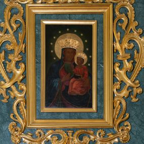 Zdjęcie nr 1: Obraz uzyskał kształt stojącego prostokąta ujętego w proste, złocone i profilowane ramy oraz dekoracyjne obramienie utworzone z płaskorzeźbionego ornamentu małżowinowo-chrząstkowego przytwierdzonego do zielono-błękitnego marmurowego tła. W zwieńczeniu obramienia kartusz z napisem: AVE MARIA. W centrum kompozycji na ciemnym, jednolitym tle ukazano frontalnie Madonnę z Dzieciątkiem w typie Matki Boskiej Częstochowskiej. Maria na lewym przedramieniu trzyma Dzieciątko Jezus, na które wskazuje prawą ręką przyłożoną do piersi. Matka Boska ma pociągłą twarz o brązowej karnacji z wyraźnie zaznaczonymi drobnymi ustami o pełnych wargach, wydatnym nosie i małych, migdałowych, otwartych oczach. Na jej prawym policzku widoczne są dwie rysy. Madonna ubrana jest w ciemnoniebieski maforion podbity czerwienią i lamowany taśmą z malarskim naśladownictwem kameryzacji. Spod maforionu widoczna jest zielona, marszczona suknia obwiedziona pod szyją taśmą także z malarskim naśladownictwem kameryzacji. Siedzące Dzieciątko Jezus zostało ujęte w trzech czwartych w prawo. Prawą rękę unosi w geście błogosławieństwa, lewą zaś podtrzymuje na kolanach zamknięty na dwie klamry kodeks. Jezus o jasnobrązowej karnacji ma owalną twarz o spojrzeniu skierowanym na matkę, mały nos i pełne usta. Jego głowę otaczają kędzierzawe, brązowe włosy rozjaśnione przy końcówkach loków. Ubrany jest w czerwoną, marszczoną na piersi tunikę lamowaną pod szyją, u spodu i przy rękawach taśmą z malarskim naśladownictwem kameryzacji. Spod tuniki wdać na dole jego bosą stopę. Głowy obu postaci otaczają złocone nimby oraz dwanaście malowanych gwiazd, na które nałożono mniejsze, metalowe i złocone. Na głowach Marii i Jezusa nałożone są srebrne i złocone korony o floranych sterczynach zdobione kameryzacją.    
