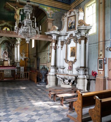 Zdjęcie nr 2: Przyścienny ołtarz Matki Boskiej Częstochowskiej uzyskał formę architektonicznej nastawy jednokondygnacyjnej, jednoosiowej ze zwieńczeniem. Drewniana mensa z portatylem flankowana przez dwustrefowy wklęsło-wypukły cokół wspiera się na ażurowym, konsolowym stipesie ołtarzowym, dekorowanym ornamentami rocalliowymi. Kondygnacja wsparta na dwustrefowym cokole została ujęta dwiema parami pilastrów zwróconych delikatnie do wewnątrz oraz silnie wysuniętą do przodu parą kolumn o kapitelach kompozytowych. Podpory dźwigają belkowanie o wklęsło-wypukłej linii. Nad polem środkowym belkowanie jest przerwane, a na osiach podpór wyłamane. Na przedłużeniu kolumn na belkowaniu usytuowano wolutowe przyczółki dekorowane rocalliem, stanowiących postumenty do skradzionych figur aniołów. W polu środkowym umieszczono obecnie obraz Matki Boskiej Nieustającej Pomocy Najświętszego, ujęty profilowaną, złoconą ramą w formie stojącego prostokąta zamkniętego łukiem półkolistym nadwieszonym z uskokiem, dekorowaną ornamentem rocalliowym. Poniżej obrazu pomiędzy dwiema rocalliowymi konsolami widnieje zdjęcie obrazu św. Jana Nepomucena. Zwieńczenie uzyskało formę leżącego prostokąta o wklęsłych, wolutowych bokach przechodzących u góry we wklęsło-wypukłe belkowanie, przyjmujące nad polem formę łuku falistego. W polu zwieńczenia znalazło się zdjęcie obrazu ze św. Józefem ujęte we wklęsło-wypukłą, profilowaną i złoconą ramę. Pilastry kondygnacji ozdobiono kapitelami z rocaille, a ich trzony udekorowano złoconymi zwisami utworzonymi z rocaille, rozet i liści. Całość struktury polichromowano na biało, a ornamenty i profile zostały wyzłocone. 