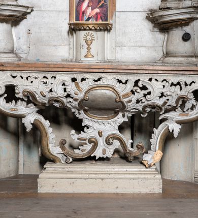 Zdjęcie nr 5: Przyścienny ołtarz Matki Boskiej Częstochowskiej uzyskał formę architektonicznej nastawy jednokondygnacyjnej, jednoosiowej ze zwieńczeniem. Drewniana mensa z portatylem flankowana przez dwustrefowy wklęsło-wypukły cokół wspiera się na ażurowym, konsolowym stipesie ołtarzowym, dekorowanym ornamentami rocalliowymi. Kondygnacja wsparta na dwustrefowym cokole została ujęta dwiema parami pilastrów zwróconych delikatnie do wewnątrz oraz silnie wysuniętą do przodu parą kolumn o kapitelach kompozytowych. Podpory dźwigają belkowanie o wklęsło-wypukłej linii. Nad polem środkowym belkowanie jest przerwane, a na osiach podpór wyłamane. Na przedłużeniu kolumn na belkowaniu usytuowano wolutowe przyczółki dekorowane rocalliem, stanowiących postumenty do skradzionych figur aniołów. W polu środkowym umieszczono obecnie obraz Matki Boskiej Nieustającej Pomocy Najświętszego, ujęty profilowaną, złoconą ramą w formie stojącego prostokąta zamkniętego łukiem półkolistym nadwieszonym z uskokiem, dekorowaną ornamentem rocalliowym. Poniżej obrazu pomiędzy dwiema rocalliowymi konsolami widnieje zdjęcie obrazu św. Jana Nepomucena. Zwieńczenie uzyskało formę leżącego prostokąta o wklęsłych, wolutowych bokach przechodzących u góry we wklęsło-wypukłe belkowanie, przyjmujące nad polem formę łuku falistego. W polu zwieńczenia znalazło się zdjęcie obrazu ze św. Józefem ujęte we wklęsło-wypukłą, profilowaną i złoconą ramę. Pilastry kondygnacji ozdobiono kapitelami z rocaille, a ich trzony udekorowano złoconymi zwisami utworzonymi z rocaille, rozet i liści. Całość struktury polichromowano na biało, a ornamenty i profile zostały wyzłocone. 