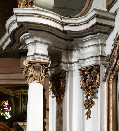 Zdjęcie nr 9: Przyścienny ołtarz Matki Boskiej Częstochowskiej uzyskał formę architektonicznej nastawy jednokondygnacyjnej, jednoosiowej ze zwieńczeniem. Drewniana mensa z portatylem flankowana przez dwustrefowy wklęsło-wypukły cokół wspiera się na ażurowym, konsolowym stipesie ołtarzowym, dekorowanym ornamentami rocalliowymi. Kondygnacja wsparta na dwustrefowym cokole została ujęta dwiema parami pilastrów zwróconych delikatnie do wewnątrz oraz silnie wysuniętą do przodu parą kolumn o kapitelach kompozytowych. Podpory dźwigają belkowanie o wklęsło-wypukłej linii. Nad polem środkowym belkowanie jest przerwane, a na osiach podpór wyłamane. Na przedłużeniu kolumn na belkowaniu usytuowano wolutowe przyczółki dekorowane rocalliem, stanowiących postumenty do skradzionych figur aniołów. W polu środkowym umieszczono obecnie obraz Matki Boskiej Nieustającej Pomocy Najświętszego, ujęty profilowaną, złoconą ramą w formie stojącego prostokąta zamkniętego łukiem półkolistym nadwieszonym z uskokiem, dekorowaną ornamentem rocalliowym. Poniżej obrazu pomiędzy dwiema rocalliowymi konsolami widnieje zdjęcie obrazu św. Jana Nepomucena. Zwieńczenie uzyskało formę leżącego prostokąta o wklęsłych, wolutowych bokach przechodzących u góry we wklęsło-wypukłe belkowanie, przyjmujące nad polem formę łuku falistego. W polu zwieńczenia znalazło się zdjęcie obrazu ze św. Józefem ujęte we wklęsło-wypukłą, profilowaną i złoconą ramę. Pilastry kondygnacji ozdobiono kapitelami z rocaille, a ich trzony udekorowano złoconymi zwisami utworzonymi z rocaille, rozet i liści. Całość struktury polichromowano na biało, a ornamenty i profile zostały wyzłocone. 