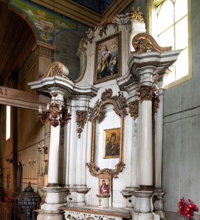 Zdjęcie nr 1: Przyścienny ołtarz Matki Boskiej Częstochowskiej uzyskał formę architektonicznej nastawy jednokondygnacyjnej, jednoosiowej ze zwieńczeniem. Drewniana mensa z portatylem flankowana przez dwustrefowy wklęsło-wypukły cokół wspiera się na ażurowym, konsolowym stipesie ołtarzowym, dekorowanym ornamentami rocalliowymi. Kondygnacja wsparta na dwustrefowym cokole została ujęta dwiema parami pilastrów zwróconych delikatnie do wewnątrz oraz silnie wysuniętą do przodu parą kolumn o kapitelach kompozytowych. Podpory dźwigają belkowanie o wklęsło-wypukłej linii. Nad polem środkowym belkowanie jest przerwane, a na osiach podpór wyłamane. Na przedłużeniu kolumn na belkowaniu usytuowano wolutowe przyczółki dekorowane rocalliem, stanowiących postumenty do skradzionych figur aniołów. W polu środkowym umieszczono obecnie obraz Matki Boskiej Nieustającej Pomocy Najświętszego, ujęty profilowaną, złoconą ramą w formie stojącego prostokąta zamkniętego łukiem półkolistym nadwieszonym z uskokiem, dekorowaną ornamentem rocalliowym. Poniżej obrazu pomiędzy dwiema rocalliowymi konsolami widnieje zdjęcie obrazu św. Jana Nepomucena. Zwieńczenie uzyskało formę leżącego prostokąta o wklęsłych, wolutowych bokach przechodzących u góry we wklęsło-wypukłe belkowanie, przyjmujące nad polem formę łuku falistego. W polu zwieńczenia znalazło się zdjęcie obrazu ze św. Józefem ujęte we wklęsło-wypukłą, profilowaną i złoconą ramę. Pilastry kondygnacji ozdobiono kapitelami z rocaille, a ich trzony udekorowano złoconymi zwisami utworzonymi z rocaille, rozet i liści. Całość struktury polichromowano na biało, a ornamenty i profile zostały wyzłocone. 