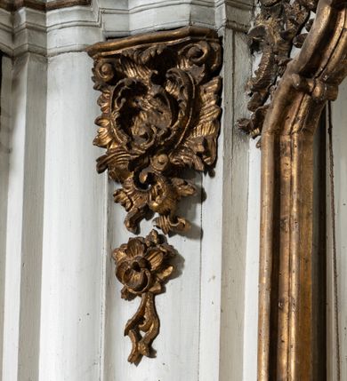 Zdjęcie nr 10: Przyścienny ołtarz Matki Boskiej Częstochowskiej uzyskał formę architektonicznej nastawy jednokondygnacyjnej, jednoosiowej ze zwieńczeniem. Drewniana mensa z portatylem flankowana przez dwustrefowy wklęsło-wypukły cokół wspiera się na ażurowym, konsolowym stipesie ołtarzowym, dekorowanym ornamentami rocalliowymi. Kondygnacja wsparta na dwustrefowym cokole została ujęta dwiema parami pilastrów zwróconych delikatnie do wewnątrz oraz silnie wysuniętą do przodu parą kolumn o kapitelach kompozytowych. Podpory dźwigają belkowanie o wklęsło-wypukłej linii. Nad polem środkowym belkowanie jest przerwane, a na osiach podpór wyłamane. Na przedłużeniu kolumn na belkowaniu usytuowano wolutowe przyczółki dekorowane rocalliem, stanowiących postumenty do skradzionych figur aniołów. W polu środkowym umieszczono obecnie obraz Matki Boskiej Nieustającej Pomocy Najświętszego, ujęty profilowaną, złoconą ramą w formie stojącego prostokąta zamkniętego łukiem półkolistym nadwieszonym z uskokiem, dekorowaną ornamentem rocalliowym. Poniżej obrazu pomiędzy dwiema rocalliowymi konsolami widnieje zdjęcie obrazu św. Jana Nepomucena. Zwieńczenie uzyskało formę leżącego prostokąta o wklęsłych, wolutowych bokach przechodzących u góry we wklęsło-wypukłe belkowanie, przyjmujące nad polem formę łuku falistego. W polu zwieńczenia znalazło się zdjęcie obrazu ze św. Józefem ujęte we wklęsło-wypukłą, profilowaną i złoconą ramę. Pilastry kondygnacji ozdobiono kapitelami z rocaille, a ich trzony udekorowano złoconymi zwisami utworzonymi z rocaille, rozet i liści. Całość struktury polichromowano na biało, a ornamenty i profile zostały wyzłocone. 