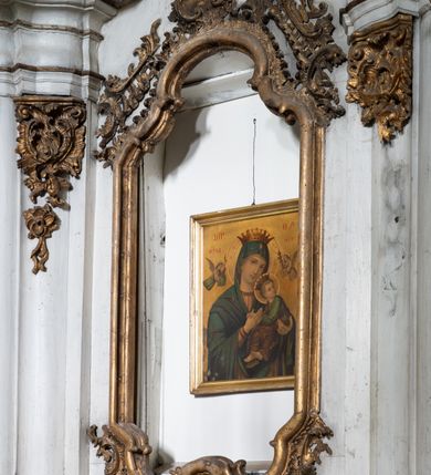 Zdjęcie nr 8: Przyścienny ołtarz Matki Boskiej Częstochowskiej uzyskał formę architektonicznej nastawy jednokondygnacyjnej, jednoosiowej ze zwieńczeniem. Drewniana mensa z portatylem flankowana przez dwustrefowy wklęsło-wypukły cokół wspiera się na ażurowym, konsolowym stipesie ołtarzowym, dekorowanym ornamentami rocalliowymi. Kondygnacja wsparta na dwustrefowym cokole została ujęta dwiema parami pilastrów zwróconych delikatnie do wewnątrz oraz silnie wysuniętą do przodu parą kolumn o kapitelach kompozytowych. Podpory dźwigają belkowanie o wklęsło-wypukłej linii. Nad polem środkowym belkowanie jest przerwane, a na osiach podpór wyłamane. Na przedłużeniu kolumn na belkowaniu usytuowano wolutowe przyczółki dekorowane rocalliem, stanowiących postumenty do skradzionych figur aniołów. W polu środkowym umieszczono obecnie obraz Matki Boskiej Nieustającej Pomocy Najświętszego, ujęty profilowaną, złoconą ramą w formie stojącego prostokąta zamkniętego łukiem półkolistym nadwieszonym z uskokiem, dekorowaną ornamentem rocalliowym. Poniżej obrazu pomiędzy dwiema rocalliowymi konsolami widnieje zdjęcie obrazu św. Jana Nepomucena. Zwieńczenie uzyskało formę leżącego prostokąta o wklęsłych, wolutowych bokach przechodzących u góry we wklęsło-wypukłe belkowanie, przyjmujące nad polem formę łuku falistego. W polu zwieńczenia znalazło się zdjęcie obrazu ze św. Józefem ujęte we wklęsło-wypukłą, profilowaną i złoconą ramę. Pilastry kondygnacji ozdobiono kapitelami z rocaille, a ich trzony udekorowano złoconymi zwisami utworzonymi z rocaille, rozet i liści. Całość struktury polichromowano na biało, a ornamenty i profile zostały wyzłocone. 