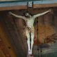 Zdjęcie nr 1: Rzeźbioną postać Ukrzyżowanego Chrystusa została umieszczona na drewnianym krzyżu, którego górne ramię wieńczy biały titulus w formie krótkiej banderoli z napisem: &quot;I.N. / R.I&quot;. Ciało Chrystusa wisi na lekko opadniętych ramionach. Głowa Zbawiciela opada na jego prawe ramię. Chrystus ma pociągłą twarz okoloną kędzierzawą brodą oraz mocno pofalowanymi, ciemnymi włosami spływającymi na ramiona, odsłaniającymi jego lewe ucho. Na głowie ma koronę cierniową uplecioną z gęstych gałązek ciernia. Spod korony spływają na szyję i tułów strużki krwi. Anatomicznie ukształtowany tors wyraźnie ukazuje układ żeber oraz intensywna wybroczynę przebitego prawego boku. Nogi Zbawiciela, skrzyżowana jedna na drugiej, do krzyża zostały przytwierdzone jednym gwoździem, podobnie jak i obie dłonie. Biodra Jezusa okala złocone perizonium przerzucone przez sznur, z widocznym festonem przy prawym boku. Całość rzeźby pokryto naturalistyczną polichromią. 