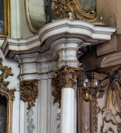 Zdjęcie nr 6: Przyścienny ołtarz Najświętszego Serca Pana Jezusa uzyskał formę architektonicznej nastawy jednokondygnacyjnej, jednoosiowej ze zwieńczeniem. Drewniana mensa z portatylem flankowana przez dwustrefowy wklęsło-wypukły cokół retabulum pierwotnie wspierała się na ażurowym, konsolowym stipesie ołtarzowym, dekorowanym ornamentami rocalliowymi. Kondygnacja wsparta na dwustrefowym cokole została ujęta dwiema parami pilastrów zwróconych delikatnie do wewnątrz oraz silnie wysuniętą do przodu parą kolumn o kapitelach kompozytowych. Podpory dźwigają belkowanie o wklęsło-wypukłej linii. Nad polem środkowym belkowanie jest przerwane, a na osiach podpór wyłamane. Na przedłużeniu kolumn na belkowaniu usytuowano wolutowe przyczółki dekorowane rocalliem, stanowiących postumenty do skradzionych figur aniołów. W polu środkowym umieszczono obraz Najświętszego Serca Pana Jezusa, ujęty profilowaną, złoconą ramą w formie stojącego prostokąta zamkniętego łukiem półkolistym nadwieszonym z uskokiem. Poniżej obrazu pomiędzy dwiema rocalliowymi konsolami widnieje zdjęcie obrazu św. Katarzyny Aleksandryjskiej. Zwieńczenie uzyskało formę leżącego prostokąta o wklęsłych, wolutowych bokach przechodzących u góry we wklęsło-wypukłe belkowanie, przyjmujące nad polem formę łuku falistego. W polu zwieńczenia znalazło się zdjęcie obrazu ze św. Sebastianem ujęte we wklęsło-wypukłą, profilowaną i złoconą ramę. Na szczycie w rocalliowym kartuszu wyobrażono złocony chrystogram "IHS" w srebrnym polu. Pilastry kondygnacji ozdobiono kapitelami z rocaille, a ich trzony udekorowano złoconymi zwisami utworzonymi z rocaille, rozet i liści. Całość struktury polichromowano na biało, a ornamenty i profile zostały wyzłocone. 