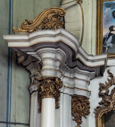 Zdjęcie nr 7: Przyścienny ołtarz Najświętszego Serca Pana Jezusa uzyskał formę architektonicznej nastawy jednokondygnacyjnej, jednoosiowej ze zwieńczeniem. Drewniana mensa z portatylem flankowana przez dwustrefowy wklęsło-wypukły cokół retabulum pierwotnie wspierała się na ażurowym, konsolowym stipesie ołtarzowym, dekorowanym ornamentami rocalliowymi. Kondygnacja wsparta na dwustrefowym cokole została ujęta dwiema parami pilastrów zwróconych delikatnie do wewnątrz oraz silnie wysuniętą do przodu parą kolumn o kapitelach kompozytowych. Podpory dźwigają belkowanie o wklęsło-wypukłej linii. Nad polem środkowym belkowanie jest przerwane, a na osiach podpór wyłamane. Na przedłużeniu kolumn na belkowaniu usytuowano wolutowe przyczółki dekorowane rocalliem, stanowiących postumenty do skradzionych figur aniołów. W polu środkowym umieszczono obraz Najświętszego Serca Pana Jezusa, ujęty profilowaną, złoconą ramą w formie stojącego prostokąta zamkniętego łukiem półkolistym nadwieszonym z uskokiem. Poniżej obrazu pomiędzy dwiema rocalliowymi konsolami widnieje zdjęcie obrazu św. Katarzyny Aleksandryjskiej. Zwieńczenie uzyskało formę leżącego prostokąta o wklęsłych, wolutowych bokach przechodzących u góry we wklęsło-wypukłe belkowanie, przyjmujące nad polem formę łuku falistego. W polu zwieńczenia znalazło się zdjęcie obrazu ze św. Sebastianem ujęte we wklęsło-wypukłą, profilowaną i złoconą ramę. Na szczycie w rocalliowym kartuszu wyobrażono złocony chrystogram "IHS" w srebrnym polu. Pilastry kondygnacji ozdobiono kapitelami z rocaille, a ich trzony udekorowano złoconymi zwisami utworzonymi z rocaille, rozet i liści. Całość struktury polichromowano na biało, a ornamenty i profile zostały wyzłocone. 