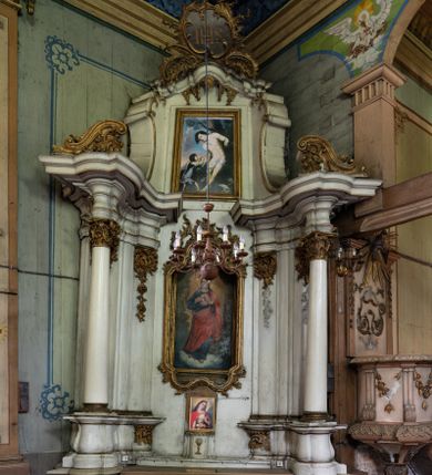 Zdjęcie nr 1: Przyścienny ołtarz Najświętszego Serca Pana Jezusa uzyskał formę architektonicznej nastawy jednokondygnacyjnej, jednoosiowej ze zwieńczeniem. Drewniana mensa z portatylem flankowana przez dwustrefowy wklęsło-wypukły cokół retabulum pierwotnie wspierała się na ażurowym, konsolowym stipesie ołtarzowym, dekorowanym ornamentami rocalliowymi. Kondygnacja wsparta na dwustrefowym cokole została ujęta dwiema parami pilastrów zwróconych delikatnie do wewnątrz oraz silnie wysuniętą do przodu parą kolumn o kapitelach kompozytowych. Podpory dźwigają belkowanie o wklęsło-wypukłej linii. Nad polem środkowym belkowanie jest przerwane, a na osiach podpór wyłamane. Na przedłużeniu kolumn na belkowaniu usytuowano wolutowe przyczółki dekorowane rocalliem, stanowiących postumenty do skradzionych figur aniołów. W polu środkowym umieszczono obraz Najświętszego Serca Pana Jezusa, ujęty profilowaną, złoconą ramą w formie stojącego prostokąta zamkniętego łukiem półkolistym nadwieszonym z uskokiem. Poniżej obrazu pomiędzy dwiema rocalliowymi konsolami widnieje zdjęcie obrazu św. Katarzyny Aleksandryjskiej. Zwieńczenie uzyskało formę leżącego prostokąta o wklęsłych, wolutowych bokach przechodzących u góry we wklęsło-wypukłe belkowanie, przyjmujące nad polem formę łuku falistego. W polu zwieńczenia znalazło się zdjęcie obrazu ze św. Sebastianem ujęte we wklęsło-wypukłą, profilowaną i złoconą ramę. Na szczycie w rocalliowym kartuszu wyobrażono złocony chrystogram "IHS" w srebrnym polu. Pilastry kondygnacji ozdobiono kapitelami z rocaille, a ich trzony udekorowano złoconymi zwisami utworzonymi z rocaille, rozet i liści. Całość struktury polichromowano na biało, a ornamenty i profile zostały wyzłocone. 