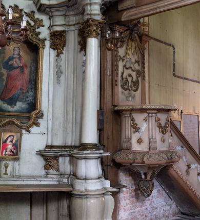 Zdjęcie nr 5: Przyścienny ołtarz Najświętszego Serca Pana Jezusa uzyskał formę architektonicznej nastawy jednokondygnacyjnej, jednoosiowej ze zwieńczeniem. Drewniana mensa z portatylem flankowana przez dwustrefowy wklęsło-wypukły cokół retabulum pierwotnie wspierała się na ażurowym, konsolowym stipesie ołtarzowym, dekorowanym ornamentami rocalliowymi. Kondygnacja wsparta na dwustrefowym cokole została ujęta dwiema parami pilastrów zwróconych delikatnie do wewnątrz oraz silnie wysuniętą do przodu parą kolumn o kapitelach kompozytowych. Podpory dźwigają belkowanie o wklęsło-wypukłej linii. Nad polem środkowym belkowanie jest przerwane, a na osiach podpór wyłamane. Na przedłużeniu kolumn na belkowaniu usytuowano wolutowe przyczółki dekorowane rocalliem, stanowiących postumenty do skradzionych figur aniołów. W polu środkowym umieszczono obraz Najświętszego Serca Pana Jezusa, ujęty profilowaną, złoconą ramą w formie stojącego prostokąta zamkniętego łukiem półkolistym nadwieszonym z uskokiem. Poniżej obrazu pomiędzy dwiema rocalliowymi konsolami widnieje zdjęcie obrazu św. Katarzyny Aleksandryjskiej. Zwieńczenie uzyskało formę leżącego prostokąta o wklęsłych, wolutowych bokach przechodzących u góry we wklęsło-wypukłe belkowanie, przyjmujące nad polem formę łuku falistego. W polu zwieńczenia znalazło się zdjęcie obrazu ze św. Sebastianem ujęte we wklęsło-wypukłą, profilowaną i złoconą ramę. Na szczycie w rocalliowym kartuszu wyobrażono złocony chrystogram "IHS" w srebrnym polu. Pilastry kondygnacji ozdobiono kapitelami z rocaille, a ich trzony udekorowano złoconymi zwisami utworzonymi z rocaille, rozet i liści. Całość struktury polichromowano na biało, a ornamenty i profile zostały wyzłocone. 