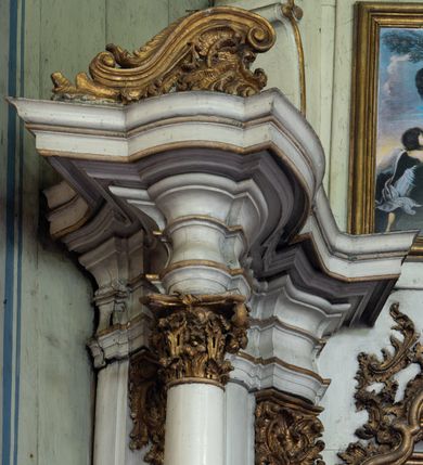 Zdjęcie nr 9: Przyścienny ołtarz Najświętszego Serca Pana Jezusa uzyskał formę architektonicznej nastawy jednokondygnacyjnej, jednoosiowej ze zwieńczeniem. Drewniana mensa z portatylem flankowana przez dwustrefowy wklęsło-wypukły cokół retabulum pierwotnie wspierała się na ażurowym, konsolowym stipesie ołtarzowym, dekorowanym ornamentami rocalliowymi. Kondygnacja wsparta na dwustrefowym cokole została ujęta dwiema parami pilastrów zwróconych delikatnie do wewnątrz oraz silnie wysuniętą do przodu parą kolumn o kapitelach kompozytowych. Podpory dźwigają belkowanie o wklęsło-wypukłej linii. Nad polem środkowym belkowanie jest przerwane, a na osiach podpór wyłamane. Na przedłużeniu kolumn na belkowaniu usytuowano wolutowe przyczółki dekorowane rocalliem, stanowiących postumenty do skradzionych figur aniołów. W polu środkowym umieszczono obraz Najświętszego Serca Pana Jezusa, ujęty profilowaną, złoconą ramą w formie stojącego prostokąta zamkniętego łukiem półkolistym nadwieszonym z uskokiem. Poniżej obrazu pomiędzy dwiema rocalliowymi konsolami widnieje zdjęcie obrazu św. Katarzyny Aleksandryjskiej. Zwieńczenie uzyskało formę leżącego prostokąta o wklęsłych, wolutowych bokach przechodzących u góry we wklęsło-wypukłe belkowanie, przyjmujące nad polem formę łuku falistego. W polu zwieńczenia znalazło się zdjęcie obrazu ze św. Sebastianem ujęte we wklęsło-wypukłą, profilowaną i złoconą ramę. Na szczycie w rocalliowym kartuszu wyobrażono złocony chrystogram "IHS" w srebrnym polu. Pilastry kondygnacji ozdobiono kapitelami z rocaille, a ich trzony udekorowano złoconymi zwisami utworzonymi z rocaille, rozet i liści. Całość struktury polichromowano na biało, a ornamenty i profile zostały wyzłocone. 