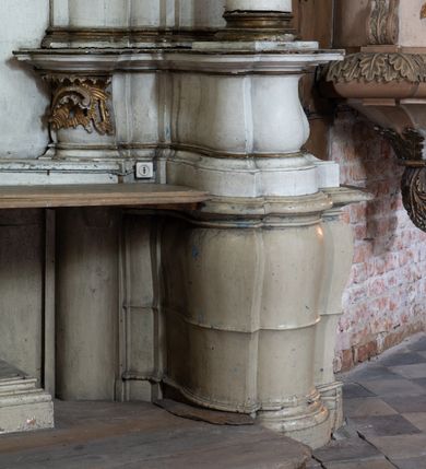 Zdjęcie nr 12: Przyścienny ołtarz Najświętszego Serca Pana Jezusa uzyskał formę architektonicznej nastawy jednokondygnacyjnej, jednoosiowej ze zwieńczeniem. Drewniana mensa z portatylem flankowana przez dwustrefowy wklęsło-wypukły cokół retabulum pierwotnie wspierała się na ażurowym, konsolowym stipesie ołtarzowym, dekorowanym ornamentami rocalliowymi. Kondygnacja wsparta na dwustrefowym cokole została ujęta dwiema parami pilastrów zwróconych delikatnie do wewnątrz oraz silnie wysuniętą do przodu parą kolumn o kapitelach kompozytowych. Podpory dźwigają belkowanie o wklęsło-wypukłej linii. Nad polem środkowym belkowanie jest przerwane, a na osiach podpór wyłamane. Na przedłużeniu kolumn na belkowaniu usytuowano wolutowe przyczółki dekorowane rocalliem, stanowiących postumenty do skradzionych figur aniołów. W polu środkowym umieszczono obraz Najświętszego Serca Pana Jezusa, ujęty profilowaną, złoconą ramą w formie stojącego prostokąta zamkniętego łukiem półkolistym nadwieszonym z uskokiem. Poniżej obrazu pomiędzy dwiema rocalliowymi konsolami widnieje zdjęcie obrazu św. Katarzyny Aleksandryjskiej. Zwieńczenie uzyskało formę leżącego prostokąta o wklęsłych, wolutowych bokach przechodzących u góry we wklęsło-wypukłe belkowanie, przyjmujące nad polem formę łuku falistego. W polu zwieńczenia znalazło się zdjęcie obrazu ze św. Sebastianem ujęte we wklęsło-wypukłą, profilowaną i złoconą ramę. Na szczycie w rocalliowym kartuszu wyobrażono złocony chrystogram "IHS" w srebrnym polu. Pilastry kondygnacji ozdobiono kapitelami z rocaille, a ich trzony udekorowano złoconymi zwisami utworzonymi z rocaille, rozet i liści. Całość struktury polichromowano na biało, a ornamenty i profile zostały wyzłocone. 