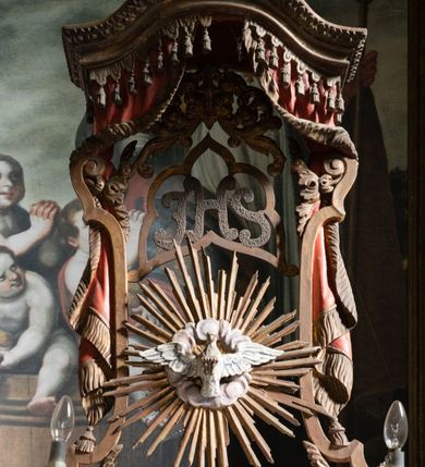 Zdjęcie nr 3: Kamienny ołtarz zamknięto w drewnianej obudowie, nakrywając go drewnianą mensą z portatylem. Stipes ołtarzowy uzyskał kształt prostopadłościanu. Antepedium ujęte zostało złoconą ramą dekorowaną rocaille’m. W jego polu umieszczono haftowaną tkaninę z medalionem w centrum z przedstawieniem w glorii chrystogramu &quot;IHS&quot;, flankowany przez wić różaną. Na mensie ołtarza usytuowano tabernakulum w formie stojącego prostopadłościanu o płaskim froncie i wklęsłych bokach pozbawionych cokołu. Drzwiczki wprawiono w płaską niszę zwieńczoną profilowanym łukiem odcinkowym, nadwieszonym. U góry tabernakulum flankuje para sakramentek. Na tabernakulum usytuowano tron eucharystyczny utworzony z dwóch ażurowych spływów wolutowych podtrzymujących baldachim z lambrekinem. Na baldachimie na czerwonej poduszce spoczywa płaska, złocona korona otwarta. Retabulum ołtarzowe wzniesiono na planie półowalu i polichromowano je na biało. Jest to architektoniczna, jednokondygnacyjna, jednoosiowa struktura ze zwieńczeniem. Po bokach flankują ją bramki ustawione na dwustrefowym, tralkowym, wklęsło-wypukłym cokole. Łuki bramek tworzą fantazyjnie wygięte dwie woluty. Kondygnacja została ujęta dwiema parami pilastrów zwróconych delikatnie do wewnątrz oraz silnie wysuniętą do przodu parą kolumn o kapitelach kompozytowych. Podpory dźwigają pełne belkowanie o wklęsło-wypukłej linii. Nad polem środkowym belkowanie jest połączone gzymsem przyjmującym formę łuku falistego i wyłamane na osiach podpór. Kondygnację ujmują spływy wolutowe połączone z łukowato wygiętymi wolutami podtrzymywanymi przez wysokie tralkowe cokoły, tworząc bramki ołtarza. Bramki zwieńczono fantazyjnie wygiętymi impostami podtrzymującymi ornament rocalliowy. W polu środkowym umieszczono wielkoformatowe zdjęcie znajdującego się tu pierwotnie obrazu św. Mikołaja, ujęte profilowaną, złoconą ramą w formie stojącego prostokąta zamkniętego łukiem półkolistym nadwieszonym z uskokiem. Zwieńczenie uzyskało formę leżącego prostokąta flankowanego parą pilastrów zwróconych do wewnątrz oraz parą pilastrów zwróconych na zewnątrz, których trzony przechodzą w spływy wolutowe opadające na belkowanie. Pilastry dźwigają niepełne, wklęsło-wypukłe belkowanie przyjmujące nad polem formę łuku falistego. W polu zwieńczenia znalazło się przedstawienie gołębicy Ducha Świętego z ażurowymi promieniami na tle owalnego okna prezbiterium, ujęte w fantazjną, wklęsło-wypukłą, profilowaną i złoconą ramę. Pilastry kondygnacji ozdobiono kapitelami z rocaille, a ich trzony udekorowano złoconymi, rokokowymi panneau ze zwisami utworzonymi z rocaille, rozet i liści. Na ich tle usytuowano pierwotnie figury św. Kazimierza Królewicza i św. Augustyna (obecnie przeniesione do krypty nowego kościoła). Rzeźby stały na górnej strefie cokołu na wspornikach z rocaille. W przyłuczach i na belkowaniu znalazły się ornamenty roślinne. Także trzony pilastrów zwieńczenia dekorowane są złoconymi zwisami z rocaille i kwiatów. Pole wokół promieni z gołębicą Ducha Świętego również ozdobiono fragmentami rocaille. 