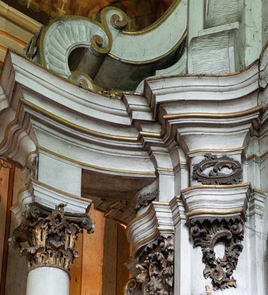 Zdjęcie nr 13: Kamienny ołtarz zamknięto w drewnianej obudowie, nakrywając go drewnianą mensą z portatylem. Stipes ołtarzowy uzyskał kształt prostopadłościanu. Antepedium ujęte zostało złoconą ramą dekorowaną rocaille’m. W jego polu umieszczono haftowaną tkaninę z medalionem w centrum z przedstawieniem w glorii chrystogramu &quot;IHS&quot;, flankowany przez wić różaną. Na mensie ołtarza usytuowano tabernakulum w formie stojącego prostopadłościanu o płaskim froncie i wklęsłych bokach pozbawionych cokołu. Drzwiczki wprawiono w płaską niszę zwieńczoną profilowanym łukiem odcinkowym, nadwieszonym. U góry tabernakulum flankuje para sakramentek. Na tabernakulum usytuowano tron eucharystyczny utworzony z dwóch ażurowych spływów wolutowych podtrzymujących baldachim z lambrekinem. Na baldachimie na czerwonej poduszce spoczywa płaska, złocona korona otwarta. Retabulum ołtarzowe wzniesiono na planie półowalu i polichromowano je na biało. Jest to architektoniczna, jednokondygnacyjna, jednoosiowa struktura ze zwieńczeniem. Po bokach flankują ją bramki ustawione na dwustrefowym, tralkowym, wklęsło-wypukłym cokole. Łuki bramek tworzą fantazyjnie wygięte dwie woluty. Kondygnacja została ujęta dwiema parami pilastrów zwróconych delikatnie do wewnątrz oraz silnie wysuniętą do przodu parą kolumn o kapitelach kompozytowych. Podpory dźwigają pełne belkowanie o wklęsło-wypukłej linii. Nad polem środkowym belkowanie jest połączone gzymsem przyjmującym formę łuku falistego i wyłamane na osiach podpór. Kondygnację ujmują spływy wolutowe połączone z łukowato wygiętymi wolutami podtrzymywanymi przez wysokie tralkowe cokoły, tworząc bramki ołtarza. Bramki zwieńczono fantazyjnie wygiętymi impostami podtrzymującymi ornament rocalliowy. W polu środkowym umieszczono wielkoformatowe zdjęcie znajdującego się tu pierwotnie obrazu św. Mikołaja, ujęte profilowaną, złoconą ramą w formie stojącego prostokąta zamkniętego łukiem półkolistym nadwieszonym z uskokiem. Zwieńczenie uzyskało formę leżącego prostokąta flankowanego parą pilastrów zwróconych do wewnątrz oraz parą pilastrów zwróconych na zewnątrz, których trzony przechodzą w spływy wolutowe opadające na belkowanie. Pilastry dźwigają niepełne, wklęsło-wypukłe belkowanie przyjmujące nad polem formę łuku falistego. W polu zwieńczenia znalazło się przedstawienie gołębicy Ducha Świętego z ażurowymi promieniami na tle owalnego okna prezbiterium, ujęte w fantazjną, wklęsło-wypukłą, profilowaną i złoconą ramę. Pilastry kondygnacji ozdobiono kapitelami z rocaille, a ich trzony udekorowano złoconymi, rokokowymi panneau ze zwisami utworzonymi z rocaille, rozet i liści. Na ich tle usytuowano pierwotnie figury św. Kazimierza Królewicza i św. Augustyna (obecnie przeniesione do krypty nowego kościoła). Rzeźby stały na górnej strefie cokołu na wspornikach z rocaille. W przyłuczach i na belkowaniu znalazły się ornamenty roślinne. Także trzony pilastrów zwieńczenia dekorowane są złoconymi zwisami z rocaille i kwiatów. Pole wokół promieni z gołębicą Ducha Świętego również ozdobiono fragmentami rocaille. 