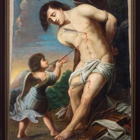 Zdjęcie nr 1: Obraz w formie stojącego prostokąta w drewnianej, profilowanej ramie. W centrum św. Sebastian przywiązany do drzewa, zwrócony w trzech czwartych w prawo, silnie pochylony, z rękami związanymi na plecach, z wysuniętą lewą nogą. Twarz ma wyrazistą, nos długi, usta lekko otwarte, oczy zamknięte, a włosy czarne. Jego nagie ciało przepasane na biodrach jest przebite czterema strzałami. Przed nim stoi anioł, który wyciąga z jego piersi strzałę. Anioł ma twarz pełną, nos krótki, usta drobne, włosy gęste, ciemne, z drobnymi puklami. Ubrany jest w luźną, niebieską suknię, odkrywającą dłonie i plecy oraz nogi. U stóp świętego leży tarcza, kołczan ze strzałami i łuk. W tle widoczne drzewa i krzewy oraz niebo. 