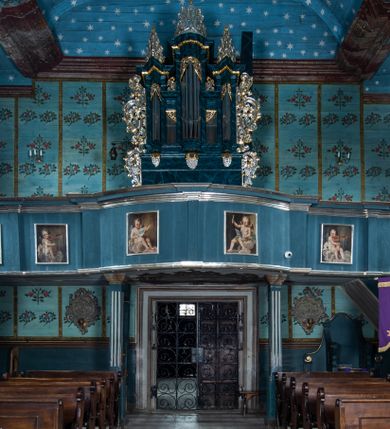 Zdjęcie nr 1: Parapet chóru muzycznego wsparty na dwóch filarach, o kanelowanych trzonach w górnej części. Balustrada o wypukłej środkowej partii, na niskim cokole, podzielona na pola pilastrami, dźwigającymi profilowany gzyms stanowiący poręcz. W polach płyciny w formie stojącego prostokąta ujętego ramą, z malowanymi przedstawieniami muzykujących aniołów siedzących na obłokach. Aniołki w kolejności od lewej strony trzymają waltornię, wiolonczelę, skrzypce, następne dwa nuty, później skrzypce, flet poprzeczny i waltornię. 