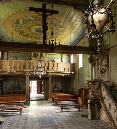 Zdjęcie nr 11: Drewniany kościół pw. św. Mikołaja w Polance jest budowlą orientowaną. Do prostokątnej nawy przylega węższe, wydłużone, trójbocznie zamknięte prezbiterium z piętrową zakrystią na osi o poligonalnym zamknięciu. Do zakrystii przylega od południa kruchta. Fragment północnej ściany prezbiterium jest murowany. Od zachodu do nawy dobudowano czworoboczną wieżę poprzedzoną przedsionkiem, który również dostawiono do nawy od południa. Prezbiterium i nawę wzniesiono na zrąb, natomiast wieżę w konstrukcji słupowej. Wieża na rzucie kwadratu posiada dwie kondygnacje. Dolna jest tej samej szerokości co nawa, górna natomiast znacznie węższa. Jej masyw podzielono smukłymi pilastrami i lizenami, zaś poniżej profilowanego gzymsu koronującego umieszczono wyrzynaną w desce koronkę. Kondygnacje oddzielono daszkiem gontowym zlewającym się po bokach z dachem kościoła. Wieżę nakryto kopulastym hełmem blaszanym, zwieńczonym blaszanym obeliskiem z krzyżem. Prezbiterium i nawę nakryto eternitowym dachem siodłowym podkreślonym profilowanym gzymsem. Nad nawą w części wschodniej zainstalowano wieżyczkę na sygnaturkę w formie wielobocznego graniastosłupa przykrytego cebulastą banią z krzyżem. Dokoła kościoła założono daszek gontowy chroniący podwaliny. Pod kościołem urządzono kryptę grzebalną. Wnętrze kościoła artykułowano za pomocą pilastrów i gzymsu. Całość nakryto stropem z fasetą. Otwór tęczowy uzyskał kształt trójlistnego, ściętego łuku, wspartego na filarkach ustawionych na profilowanej belce zawieszonej na kroksztynach. W części zachodniej nawy urządzono chór muzyczny, wsparty na dwóch kolumnach jońskich z przedpiersiem rozczłonkowanym balasami. We wnętrzu ustawiono ołtarz główny i dwa ołtarze boczne oraz ambonę, a na chórze muzycznym zainstalowano prospekt organowy.