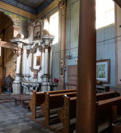 Zdjęcie nr 9: Drewniany kościół pw. św. Mikołaja w Polance jest budowlą orientowaną. Do prostokątnej nawy przylega węższe, wydłużone, trójbocznie zamknięte prezbiterium z piętrową zakrystią na osi o poligonalnym zamknięciu. Do zakrystii przylega od południa kruchta. Fragment północnej ściany prezbiterium jest murowany. Od zachodu do nawy dobudowano czworoboczną wieżę poprzedzoną przedsionkiem, który również dostawiono do nawy od południa. Prezbiterium i nawę wzniesiono na zrąb, natomiast wieżę w konstrukcji słupowej. Wieża na rzucie kwadratu posiada dwie kondygnacje. Dolna jest tej samej szerokości co nawa, górna natomiast znacznie węższa. Jej masyw podzielono smukłymi pilastrami i lizenami, zaś poniżej profilowanego gzymsu koronującego umieszczono wyrzynaną w desce koronkę. Kondygnacje oddzielono daszkiem gontowym zlewającym się po bokach z dachem kościoła. Wieżę nakryto kopulastym hełmem blaszanym, zwieńczonym blaszanym obeliskiem z krzyżem. Prezbiterium i nawę nakryto eternitowym dachem siodłowym podkreślonym profilowanym gzymsem. Nad nawą w części wschodniej zainstalowano wieżyczkę na sygnaturkę w formie wielobocznego graniastosłupa przykrytego cebulastą banią z krzyżem. Dokoła kościoła założono daszek gontowy chroniący podwaliny. Pod kościołem urządzono kryptę grzebalną. Wnętrze kościoła artykułowano za pomocą pilastrów i gzymsu. Całość nakryto stropem z fasetą. Otwór tęczowy uzyskał kształt trójlistnego, ściętego łuku, wspartego na filarkach ustawionych na profilowanej belce zawieszonej na kroksztynach. W części zachodniej nawy urządzono chór muzyczny, wsparty na dwóch kolumnach jońskich z przedpiersiem rozczłonkowanym balasami. We wnętrzu ustawiono ołtarz główny i dwa ołtarze boczne oraz ambonę, a na chórze muzycznym zainstalowano prospekt organowy.