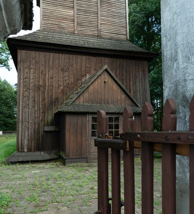 Zdjęcie nr 25: Drewniany kościół pw. św. Mikołaja w Polance jest budowlą orientowaną. Do prostokątnej nawy przylega węższe, wydłużone, trójbocznie zamknięte prezbiterium z piętrową zakrystią na osi o poligonalnym zamknięciu. Do zakrystii przylega od południa kruchta. Fragment północnej ściany prezbiterium jest murowany. Od zachodu do nawy dobudowano czworoboczną wieżę poprzedzoną przedsionkiem, który również dostawiono do nawy od południa. Prezbiterium i nawę wzniesiono na zrąb, natomiast wieżę w konstrukcji słupowej. Wieża na rzucie kwadratu posiada dwie kondygnacje. Dolna jest tej samej szerokości co nawa, górna natomiast znacznie węższa. Jej masyw podzielono smukłymi pilastrami i lizenami, zaś poniżej profilowanego gzymsu koronującego umieszczono wyrzynaną w desce koronkę. Kondygnacje oddzielono daszkiem gontowym zlewającym się po bokach z dachem kościoła. Wieżę nakryto kopulastym hełmem blaszanym, zwieńczonym blaszanym obeliskiem z krzyżem. Prezbiterium i nawę nakryto eternitowym dachem siodłowym podkreślonym profilowanym gzymsem. Nad nawą w części wschodniej zainstalowano wieżyczkę na sygnaturkę w formie wielobocznego graniastosłupa przykrytego cebulastą banią z krzyżem. Dokoła kościoła założono daszek gontowy chroniący podwaliny. Pod kościołem urządzono kryptę grzebalną. Wnętrze kościoła artykułowano za pomocą pilastrów i gzymsu. Całość nakryto stropem z fasetą. Otwór tęczowy uzyskał kształt trójlistnego, ściętego łuku, wspartego na filarkach ustawionych na profilowanej belce zawieszonej na kroksztynach. W części zachodniej nawy urządzono chór muzyczny, wsparty na dwóch kolumnach jońskich z przedpiersiem rozczłonkowanym balasami. We wnętrzu ustawiono ołtarz główny i dwa ołtarze boczne oraz ambonę, a na chórze muzycznym zainstalowano prospekt organowy.