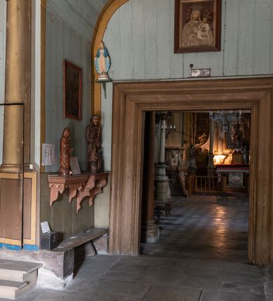 Zdjęcie nr 16: Drewniany kościół pw. św. Mikołaja w Polance jest budowlą orientowaną. Do prostokątnej nawy przylega węższe, wydłużone, trójbocznie zamknięte prezbiterium z piętrową zakrystią na osi o poligonalnym zamknięciu. Do zakrystii przylega od południa kruchta. Fragment północnej ściany prezbiterium jest murowany. Od zachodu do nawy dobudowano czworoboczną wieżę poprzedzoną przedsionkiem, który również dostawiono do nawy od południa. Prezbiterium i nawę wzniesiono na zrąb, natomiast wieżę w konstrukcji słupowej. Wieża na rzucie kwadratu posiada dwie kondygnacje. Dolna jest tej samej szerokości co nawa, górna natomiast znacznie węższa. Jej masyw podzielono smukłymi pilastrami i lizenami, zaś poniżej profilowanego gzymsu koronującego umieszczono wyrzynaną w desce koronkę. Kondygnacje oddzielono daszkiem gontowym zlewającym się po bokach z dachem kościoła. Wieżę nakryto kopulastym hełmem blaszanym, zwieńczonym blaszanym obeliskiem z krzyżem. Prezbiterium i nawę nakryto eternitowym dachem siodłowym podkreślonym profilowanym gzymsem. Nad nawą w części wschodniej zainstalowano wieżyczkę na sygnaturkę w formie wielobocznego graniastosłupa przykrytego cebulastą banią z krzyżem. Dokoła kościoła założono daszek gontowy chroniący podwaliny. Pod kościołem urządzono kryptę grzebalną. Wnętrze kościoła artykułowano za pomocą pilastrów i gzymsu. Całość nakryto stropem z fasetą. Otwór tęczowy uzyskał kształt trójlistnego, ściętego łuku, wspartego na filarkach ustawionych na profilowanej belce zawieszonej na kroksztynach. W części zachodniej nawy urządzono chór muzyczny, wsparty na dwóch kolumnach jońskich z przedpiersiem rozczłonkowanym balasami. We wnętrzu ustawiono ołtarz główny i dwa ołtarze boczne oraz ambonę, a na chórze muzycznym zainstalowano prospekt organowy.