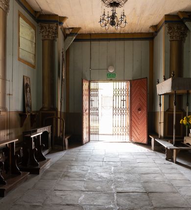 Zdjęcie nr 17: Drewniany kościół pw. św. Mikołaja w Polance jest budowlą orientowaną. Do prostokątnej nawy przylega węższe, wydłużone, trójbocznie zamknięte prezbiterium z piętrową zakrystią na osi o poligonalnym zamknięciu. Do zakrystii przylega od południa kruchta. Fragment północnej ściany prezbiterium jest murowany. Od zachodu do nawy dobudowano czworoboczną wieżę poprzedzoną przedsionkiem, który również dostawiono do nawy od południa. Prezbiterium i nawę wzniesiono na zrąb, natomiast wieżę w konstrukcji słupowej. Wieża na rzucie kwadratu posiada dwie kondygnacje. Dolna jest tej samej szerokości co nawa, górna natomiast znacznie węższa. Jej masyw podzielono smukłymi pilastrami i lizenami, zaś poniżej profilowanego gzymsu koronującego umieszczono wyrzynaną w desce koronkę. Kondygnacje oddzielono daszkiem gontowym zlewającym się po bokach z dachem kościoła. Wieżę nakryto kopulastym hełmem blaszanym, zwieńczonym blaszanym obeliskiem z krzyżem. Prezbiterium i nawę nakryto eternitowym dachem siodłowym podkreślonym profilowanym gzymsem. Nad nawą w części wschodniej zainstalowano wieżyczkę na sygnaturkę w formie wielobocznego graniastosłupa przykrytego cebulastą banią z krzyżem. Dokoła kościoła założono daszek gontowy chroniący podwaliny. Pod kościołem urządzono kryptę grzebalną. Wnętrze kościoła artykułowano za pomocą pilastrów i gzymsu. Całość nakryto stropem z fasetą. Otwór tęczowy uzyskał kształt trójlistnego, ściętego łuku, wspartego na filarkach ustawionych na profilowanej belce zawieszonej na kroksztynach. W części zachodniej nawy urządzono chór muzyczny, wsparty na dwóch kolumnach jońskich z przedpiersiem rozczłonkowanym balasami. We wnętrzu ustawiono ołtarz główny i dwa ołtarze boczne oraz ambonę, a na chórze muzycznym zainstalowano prospekt organowy.