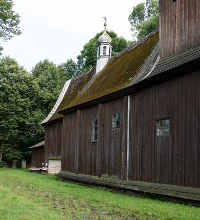 Zdjęcie nr 22: Drewniany kościół pw. św. Mikołaja w Polance jest budowlą orientowaną. Do prostokątnej nawy przylega węższe, wydłużone, trójbocznie zamknięte prezbiterium z piętrową zakrystią na osi o poligonalnym zamknięciu. Do zakrystii przylega od południa kruchta. Fragment północnej ściany prezbiterium jest murowany. Od zachodu do nawy dobudowano czworoboczną wieżę poprzedzoną przedsionkiem, który również dostawiono do nawy od południa. Prezbiterium i nawę wzniesiono na zrąb, natomiast wieżę w konstrukcji słupowej. Wieża na rzucie kwadratu posiada dwie kondygnacje. Dolna jest tej samej szerokości co nawa, górna natomiast znacznie węższa. Jej masyw podzielono smukłymi pilastrami i lizenami, zaś poniżej profilowanego gzymsu koronującego umieszczono wyrzynaną w desce koronkę. Kondygnacje oddzielono daszkiem gontowym zlewającym się po bokach z dachem kościoła. Wieżę nakryto kopulastym hełmem blaszanym, zwieńczonym blaszanym obeliskiem z krzyżem. Prezbiterium i nawę nakryto eternitowym dachem siodłowym podkreślonym profilowanym gzymsem. Nad nawą w części wschodniej zainstalowano wieżyczkę na sygnaturkę w formie wielobocznego graniastosłupa przykrytego cebulastą banią z krzyżem. Dokoła kościoła założono daszek gontowy chroniący podwaliny. Pod kościołem urządzono kryptę grzebalną. Wnętrze kościoła artykułowano za pomocą pilastrów i gzymsu. Całość nakryto stropem z fasetą. Otwór tęczowy uzyskał kształt trójlistnego, ściętego łuku, wspartego na filarkach ustawionych na profilowanej belce zawieszonej na kroksztynach. W części zachodniej nawy urządzono chór muzyczny, wsparty na dwóch kolumnach jońskich z przedpiersiem rozczłonkowanym balasami. We wnętrzu ustawiono ołtarz główny i dwa ołtarze boczne oraz ambonę, a na chórze muzycznym zainstalowano prospekt organowy.
