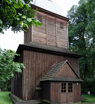Zdjęcie nr 21: Drewniany kościół pw. św. Mikołaja w Polance jest budowlą orientowaną. Do prostokątnej nawy przylega węższe, wydłużone, trójbocznie zamknięte prezbiterium z piętrową zakrystią na osi o poligonalnym zamknięciu. Do zakrystii przylega od południa kruchta. Fragment północnej ściany prezbiterium jest murowany. Od zachodu do nawy dobudowano czworoboczną wieżę poprzedzoną przedsionkiem, który również dostawiono do nawy od południa. Prezbiterium i nawę wzniesiono na zrąb, natomiast wieżę w konstrukcji słupowej. Wieża na rzucie kwadratu posiada dwie kondygnacje. Dolna jest tej samej szerokości co nawa, górna natomiast znacznie węższa. Jej masyw podzielono smukłymi pilastrami i lizenami, zaś poniżej profilowanego gzymsu koronującego umieszczono wyrzynaną w desce koronkę. Kondygnacje oddzielono daszkiem gontowym zlewającym się po bokach z dachem kościoła. Wieżę nakryto kopulastym hełmem blaszanym, zwieńczonym blaszanym obeliskiem z krzyżem. Prezbiterium i nawę nakryto eternitowym dachem siodłowym podkreślonym profilowanym gzymsem. Nad nawą w części wschodniej zainstalowano wieżyczkę na sygnaturkę w formie wielobocznego graniastosłupa przykrytego cebulastą banią z krzyżem. Dokoła kościoła założono daszek gontowy chroniący podwaliny. Pod kościołem urządzono kryptę grzebalną. Wnętrze kościoła artykułowano za pomocą pilastrów i gzymsu. Całość nakryto stropem z fasetą. Otwór tęczowy uzyskał kształt trójlistnego, ściętego łuku, wspartego na filarkach ustawionych na profilowanej belce zawieszonej na kroksztynach. W części zachodniej nawy urządzono chór muzyczny, wsparty na dwóch kolumnach jońskich z przedpiersiem rozczłonkowanym balasami. We wnętrzu ustawiono ołtarz główny i dwa ołtarze boczne oraz ambonę, a na chórze muzycznym zainstalowano prospekt organowy.