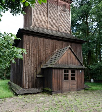 Zdjęcie nr 20: Drewniany kościół pw. św. Mikołaja w Polance jest budowlą orientowaną. Do prostokątnej nawy przylega węższe, wydłużone, trójbocznie zamknięte prezbiterium z piętrową zakrystią na osi o poligonalnym zamknięciu. Do zakrystii przylega od południa kruchta. Fragment północnej ściany prezbiterium jest murowany. Od zachodu do nawy dobudowano czworoboczną wieżę poprzedzoną przedsionkiem, który również dostawiono do nawy od południa. Prezbiterium i nawę wzniesiono na zrąb, natomiast wieżę w konstrukcji słupowej. Wieża na rzucie kwadratu posiada dwie kondygnacje. Dolna jest tej samej szerokości co nawa, górna natomiast znacznie węższa. Jej masyw podzielono smukłymi pilastrami i lizenami, zaś poniżej profilowanego gzymsu koronującego umieszczono wyrzynaną w desce koronkę. Kondygnacje oddzielono daszkiem gontowym zlewającym się po bokach z dachem kościoła. Wieżę nakryto kopulastym hełmem blaszanym, zwieńczonym blaszanym obeliskiem z krzyżem. Prezbiterium i nawę nakryto eternitowym dachem siodłowym podkreślonym profilowanym gzymsem. Nad nawą w części wschodniej zainstalowano wieżyczkę na sygnaturkę w formie wielobocznego graniastosłupa przykrytego cebulastą banią z krzyżem. Dokoła kościoła założono daszek gontowy chroniący podwaliny. Pod kościołem urządzono kryptę grzebalną. Wnętrze kościoła artykułowano za pomocą pilastrów i gzymsu. Całość nakryto stropem z fasetą. Otwór tęczowy uzyskał kształt trójlistnego, ściętego łuku, wspartego na filarkach ustawionych na profilowanej belce zawieszonej na kroksztynach. W części zachodniej nawy urządzono chór muzyczny, wsparty na dwóch kolumnach jońskich z przedpiersiem rozczłonkowanym balasami. We wnętrzu ustawiono ołtarz główny i dwa ołtarze boczne oraz ambonę, a na chórze muzycznym zainstalowano prospekt organowy.