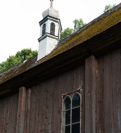 Zdjęcie nr 30: Drewniany kościół pw. św. Mikołaja w Polance jest budowlą orientowaną. Do prostokątnej nawy przylega węższe, wydłużone, trójbocznie zamknięte prezbiterium z piętrową zakrystią na osi o poligonalnym zamknięciu. Do zakrystii przylega od południa kruchta. Fragment północnej ściany prezbiterium jest murowany. Od zachodu do nawy dobudowano czworoboczną wieżę poprzedzoną przedsionkiem, który również dostawiono do nawy od południa. Prezbiterium i nawę wzniesiono na zrąb, natomiast wieżę w konstrukcji słupowej. Wieża na rzucie kwadratu posiada dwie kondygnacje. Dolna jest tej samej szerokości co nawa, górna natomiast znacznie węższa. Jej masyw podzielono smukłymi pilastrami i lizenami, zaś poniżej profilowanego gzymsu koronującego umieszczono wyrzynaną w desce koronkę. Kondygnacje oddzielono daszkiem gontowym zlewającym się po bokach z dachem kościoła. Wieżę nakryto kopulastym hełmem blaszanym, zwieńczonym blaszanym obeliskiem z krzyżem. Prezbiterium i nawę nakryto eternitowym dachem siodłowym podkreślonym profilowanym gzymsem. Nad nawą w części wschodniej zainstalowano wieżyczkę na sygnaturkę w formie wielobocznego graniastosłupa przykrytego cebulastą banią z krzyżem. Dokoła kościoła założono daszek gontowy chroniący podwaliny. Pod kościołem urządzono kryptę grzebalną. Wnętrze kościoła artykułowano za pomocą pilastrów i gzymsu. Całość nakryto stropem z fasetą. Otwór tęczowy uzyskał kształt trójlistnego, ściętego łuku, wspartego na filarkach ustawionych na profilowanej belce zawieszonej na kroksztynach. W części zachodniej nawy urządzono chór muzyczny, wsparty na dwóch kolumnach jońskich z przedpiersiem rozczłonkowanym balasami. We wnętrzu ustawiono ołtarz główny i dwa ołtarze boczne oraz ambonę, a na chórze muzycznym zainstalowano prospekt organowy.