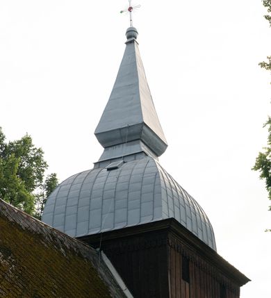 Zdjęcie nr 49: Drewniany kościół pw. św. Mikołaja w Polance jest budowlą orientowaną. Do prostokątnej nawy przylega węższe, wydłużone, trójbocznie zamknięte prezbiterium z piętrową zakrystią na osi o poligonalnym zamknięciu. Do zakrystii przylega od południa kruchta. Fragment północnej ściany prezbiterium jest murowany. Od zachodu do nawy dobudowano czworoboczną wieżę poprzedzoną przedsionkiem, który również dostawiono do nawy od południa. Prezbiterium i nawę wzniesiono na zrąb, natomiast wieżę w konstrukcji słupowej. Wieża na rzucie kwadratu posiada dwie kondygnacje. Dolna jest tej samej szerokości co nawa, górna natomiast znacznie węższa. Jej masyw podzielono smukłymi pilastrami i lizenami, zaś poniżej profilowanego gzymsu koronującego umieszczono wyrzynaną w desce koronkę. Kondygnacje oddzielono daszkiem gontowym zlewającym się po bokach z dachem kościoła. Wieżę nakryto kopulastym hełmem blaszanym, zwieńczonym blaszanym obeliskiem z krzyżem. Prezbiterium i nawę nakryto eternitowym dachem siodłowym podkreślonym profilowanym gzymsem. Nad nawą w części wschodniej zainstalowano wieżyczkę na sygnaturkę w formie wielobocznego graniastosłupa przykrytego cebulastą banią z krzyżem. Dokoła kościoła założono daszek gontowy chroniący podwaliny. Pod kościołem urządzono kryptę grzebalną. Wnętrze kościoła artykułowano za pomocą pilastrów i gzymsu. Całość nakryto stropem z fasetą. Otwór tęczowy uzyskał kształt trójlistnego, ściętego łuku, wspartego na filarkach ustawionych na profilowanej belce zawieszonej na kroksztynach. W części zachodniej nawy urządzono chór muzyczny, wsparty na dwóch kolumnach jońskich z przedpiersiem rozczłonkowanym balasami. We wnętrzu ustawiono ołtarz główny i dwa ołtarze boczne oraz ambonę, a na chórze muzycznym zainstalowano prospekt organowy.